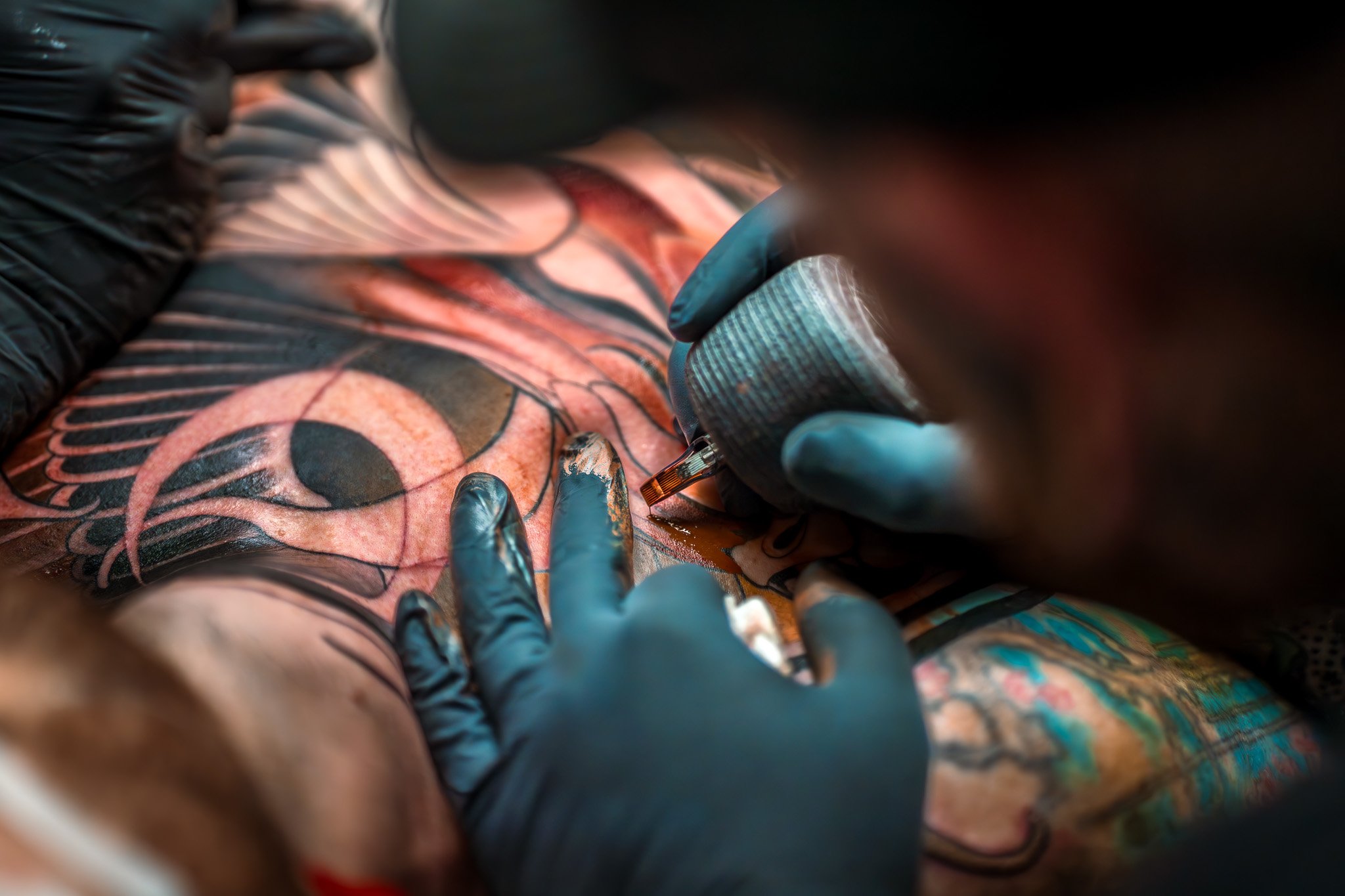 A tattoo artist working on a colorful tattoo on a person's chest, wearing black gloves and using a tattoo machine.