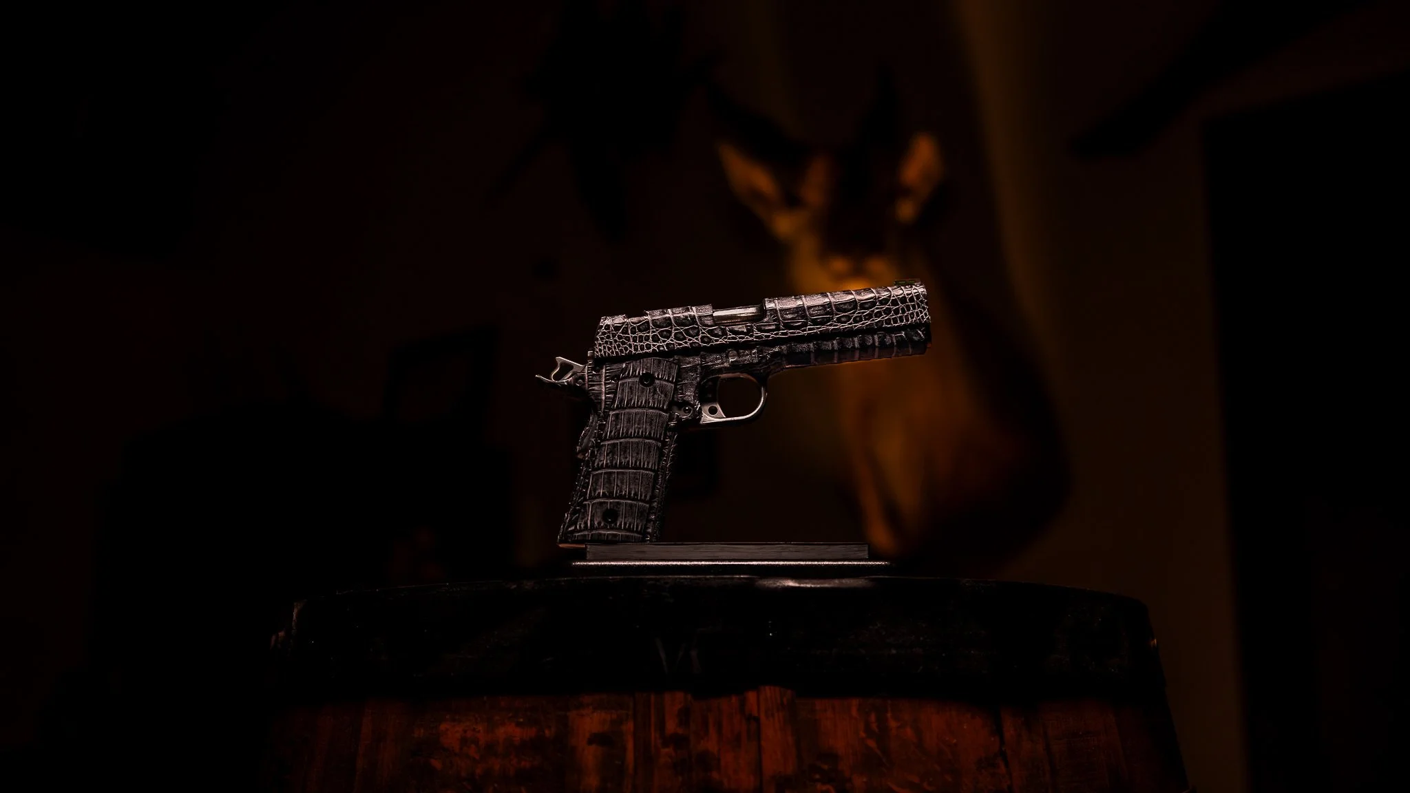 A small handgun with a black crocodile leather pattern on its surface, displayed on a stand, against a dark background.
