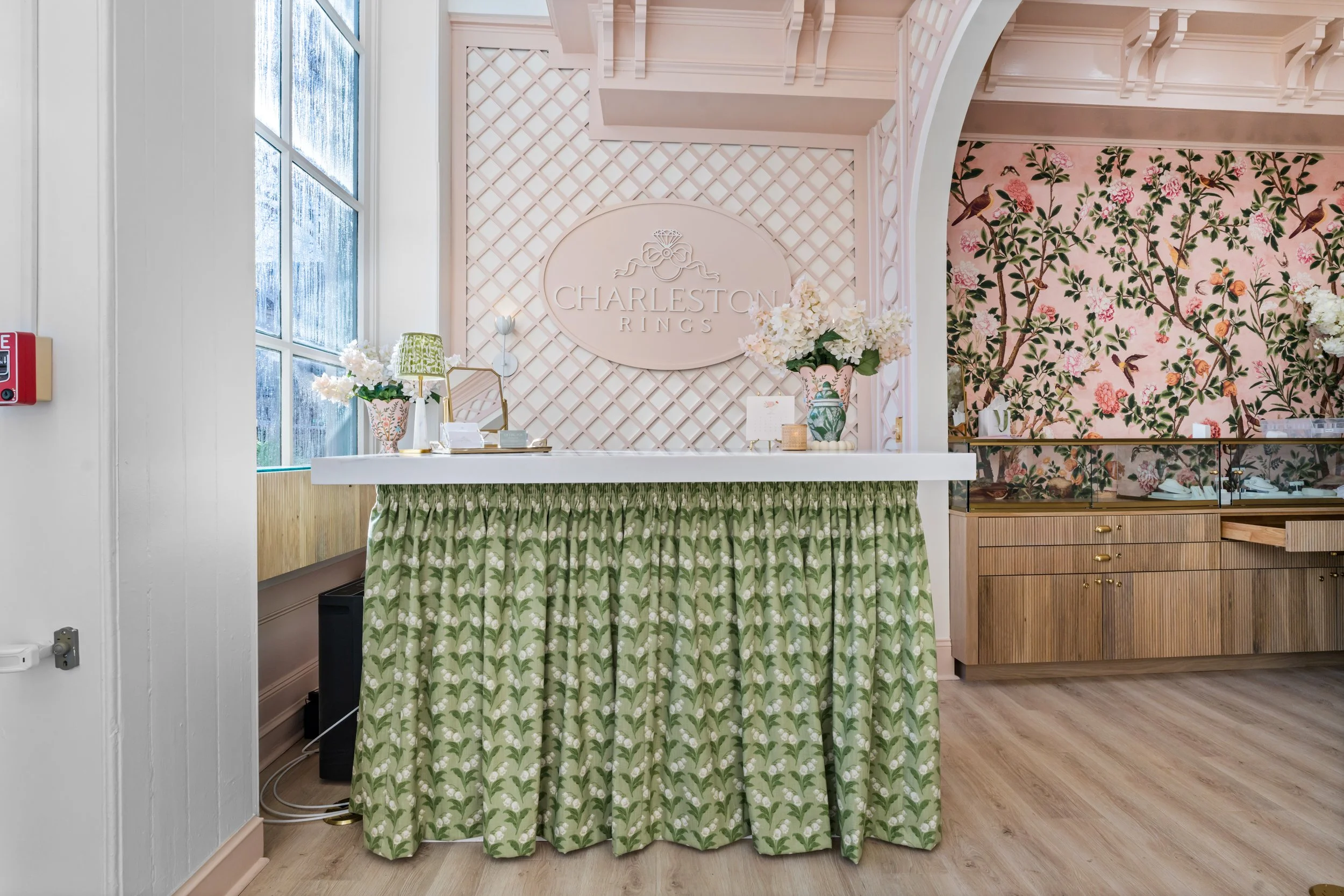 Store front desk at Charleston Rings with pink walls, floral decor, and a green and white curtain covering the front of the counter.