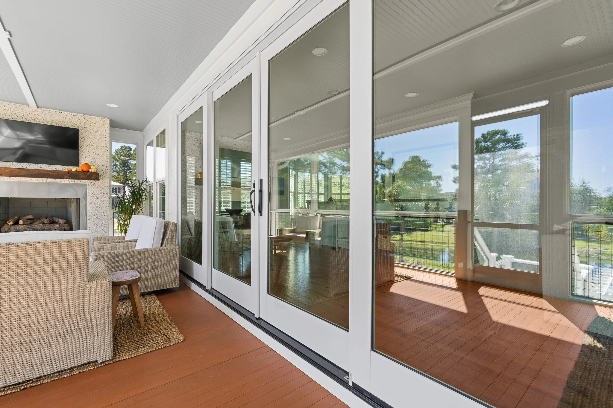 Screened porch with sliding glass doors, wicker chairs, a fireplace, and a view of trees and a grassy yard outside.