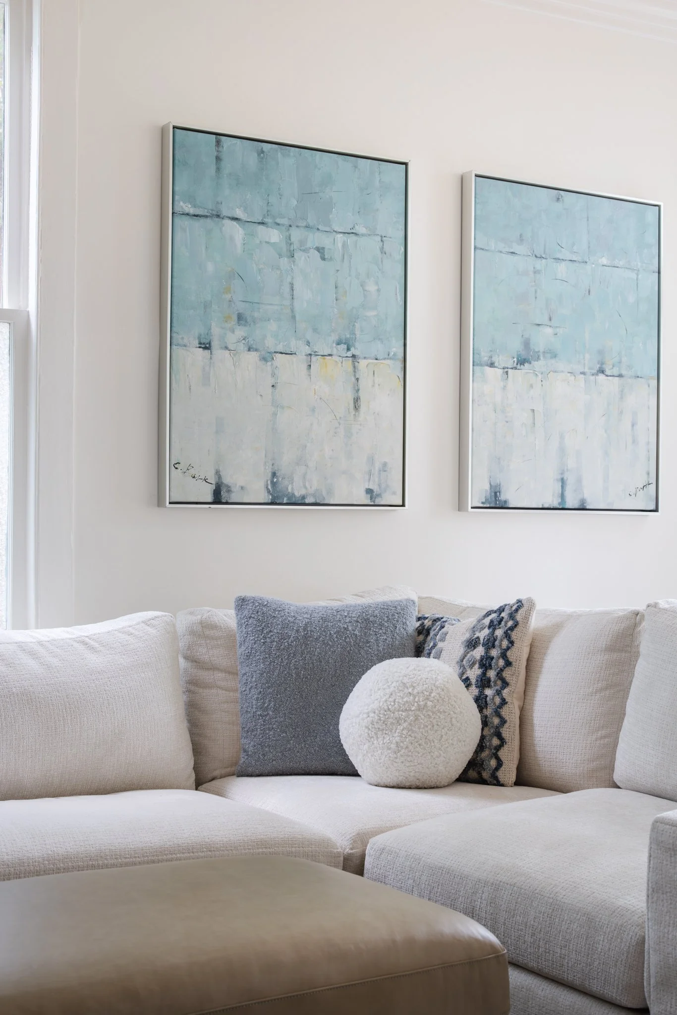 Living room with white sectional sofa, blue and white pillows, abstract blue paintings on wall