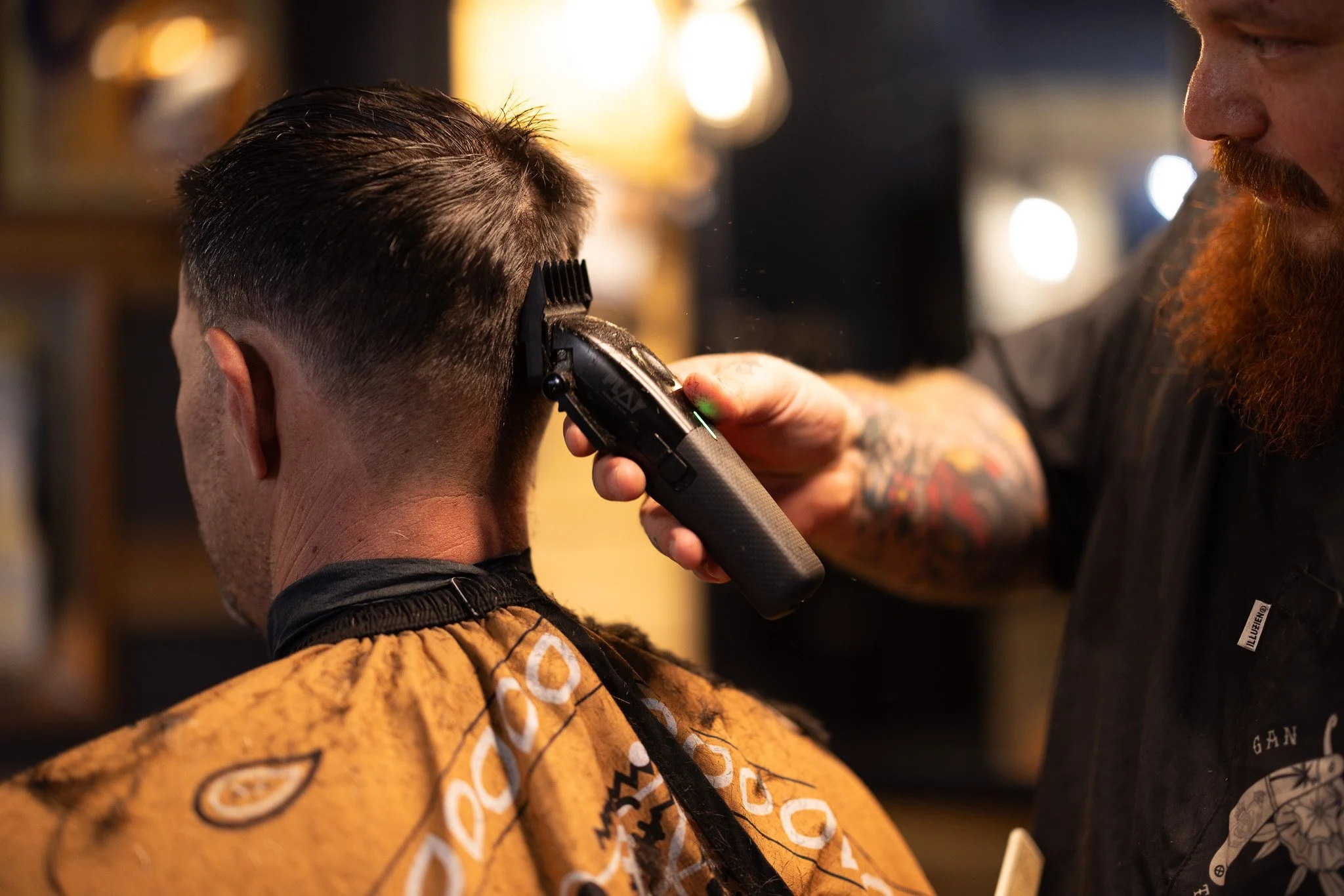 Barber giving a haircut using electric clippers in a barbershop.