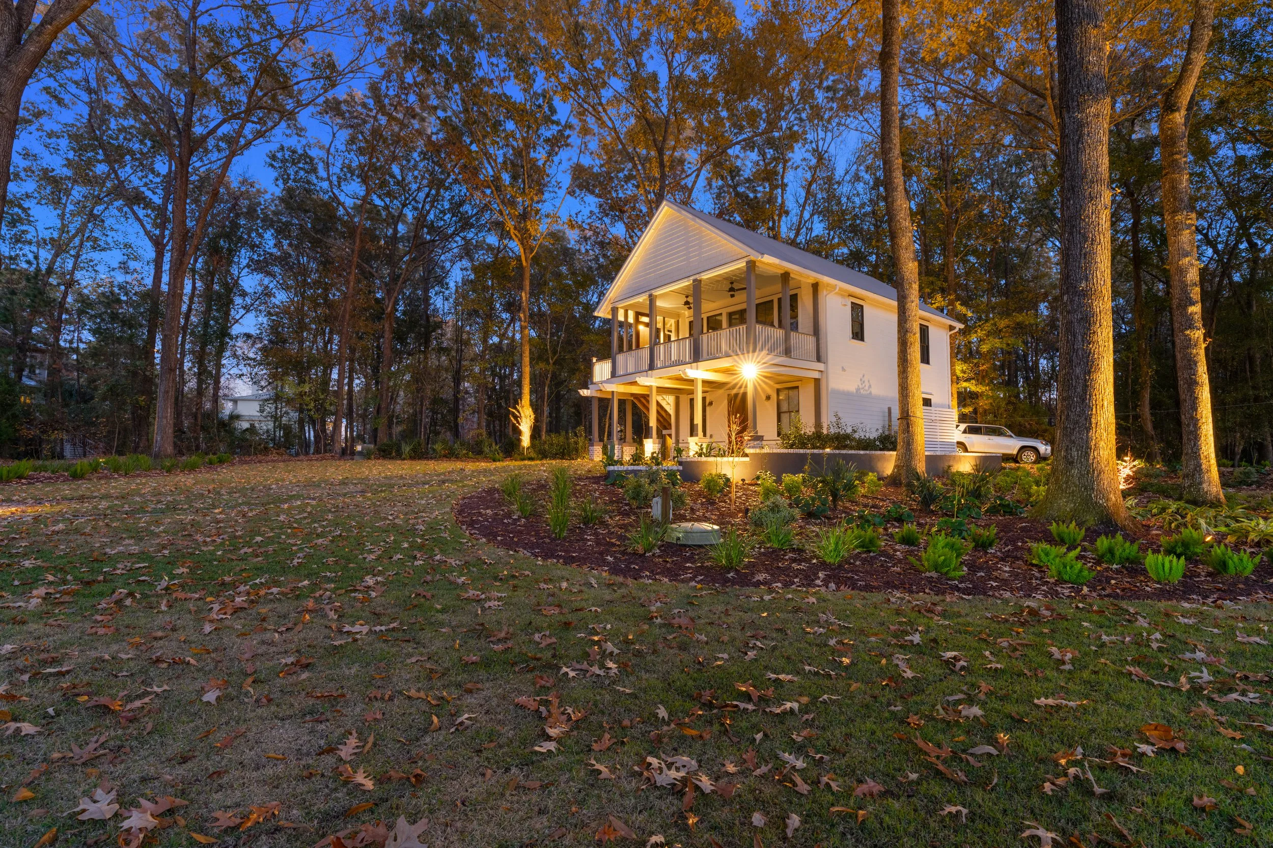 A two-story house illuminated at dusk, surrounded by trees with autumn leaves on the ground.