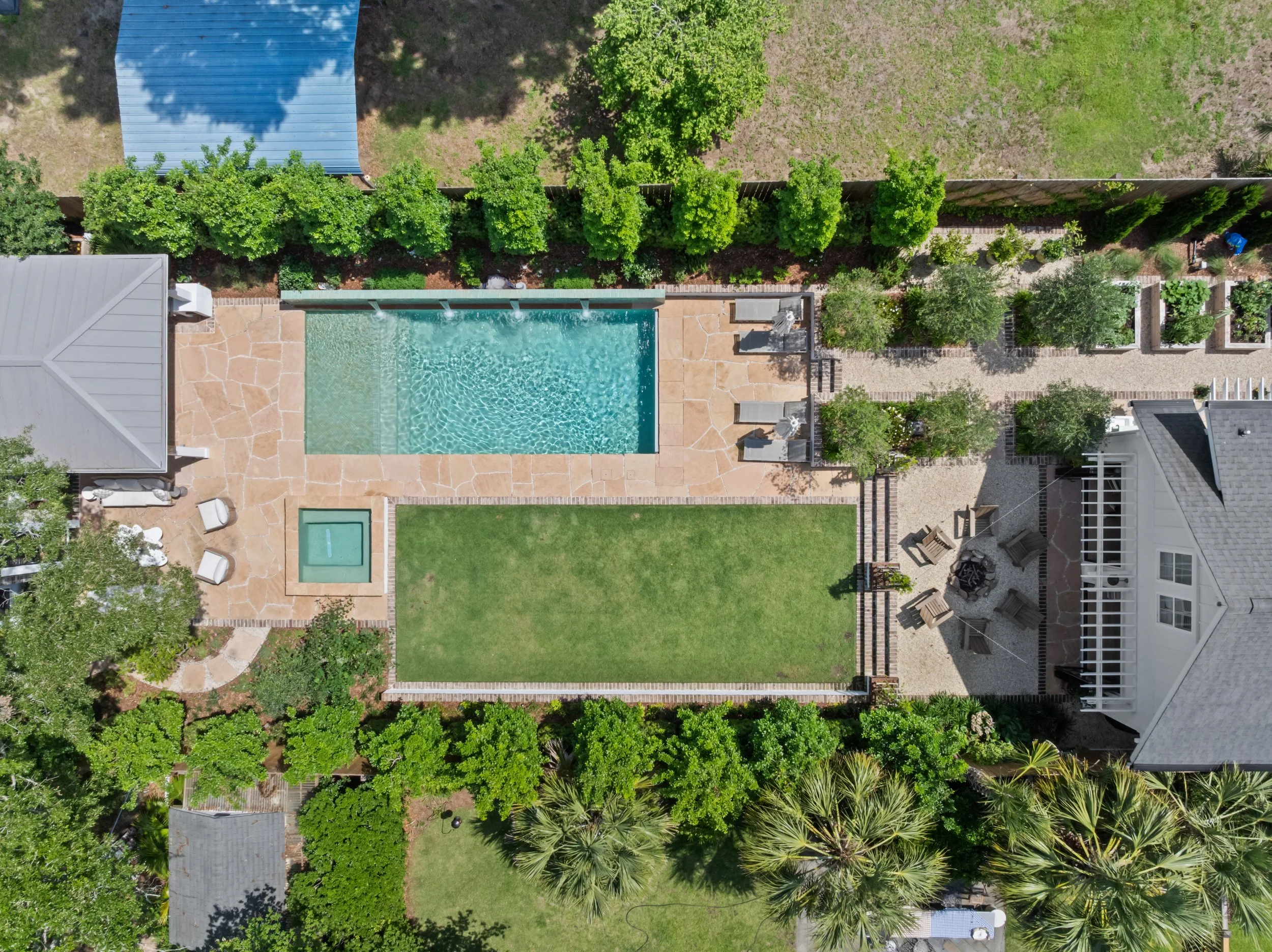 Aerial view of a backyard with a swimming pool, hot tub, lawn, patio, and surrounding trees and plants.
