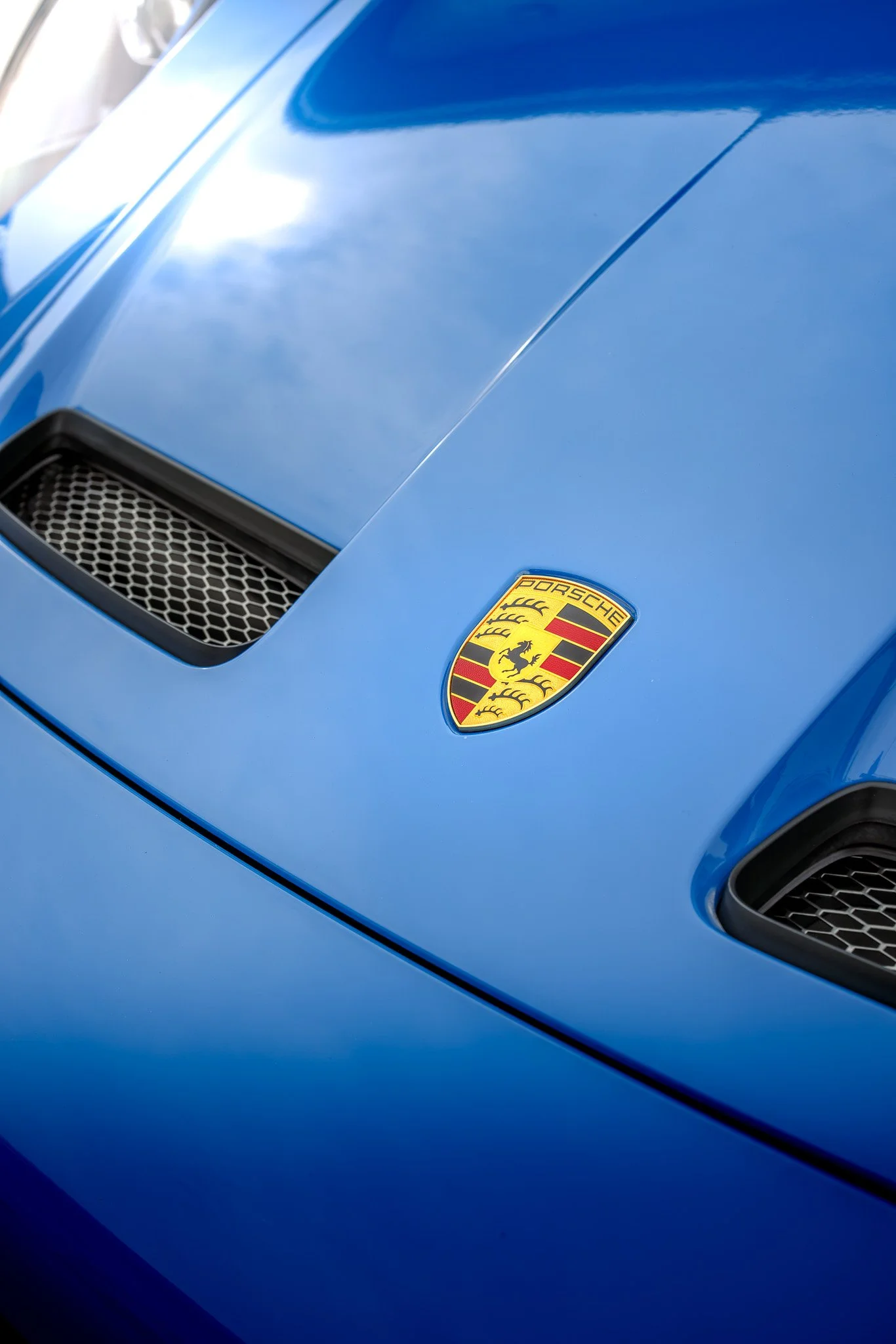 Close-up of a blue sports car hood with Porsche emblem in the center and air vents on each side.