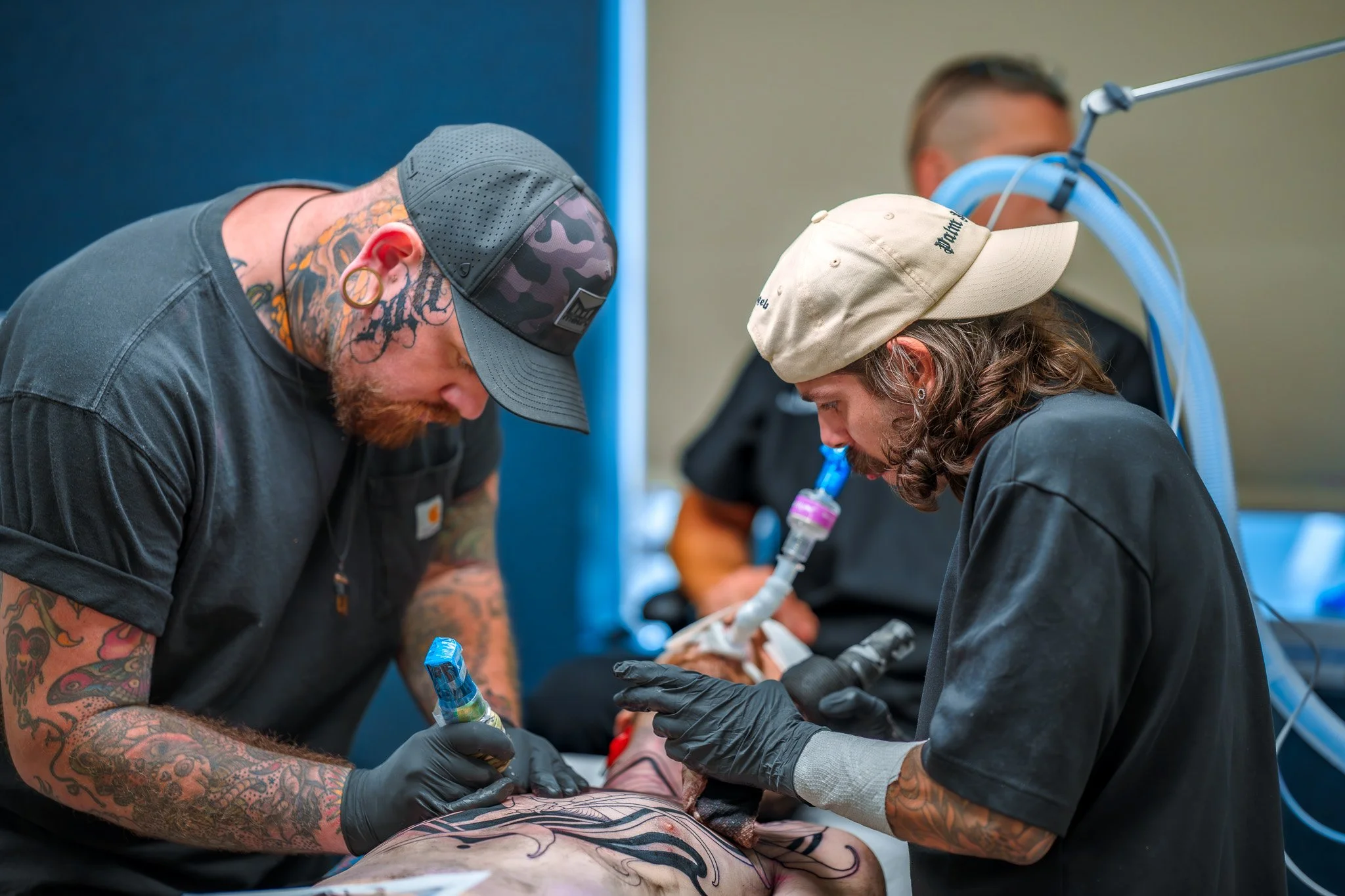 Tattoo artists working on a client during a tattooing session in a studio.