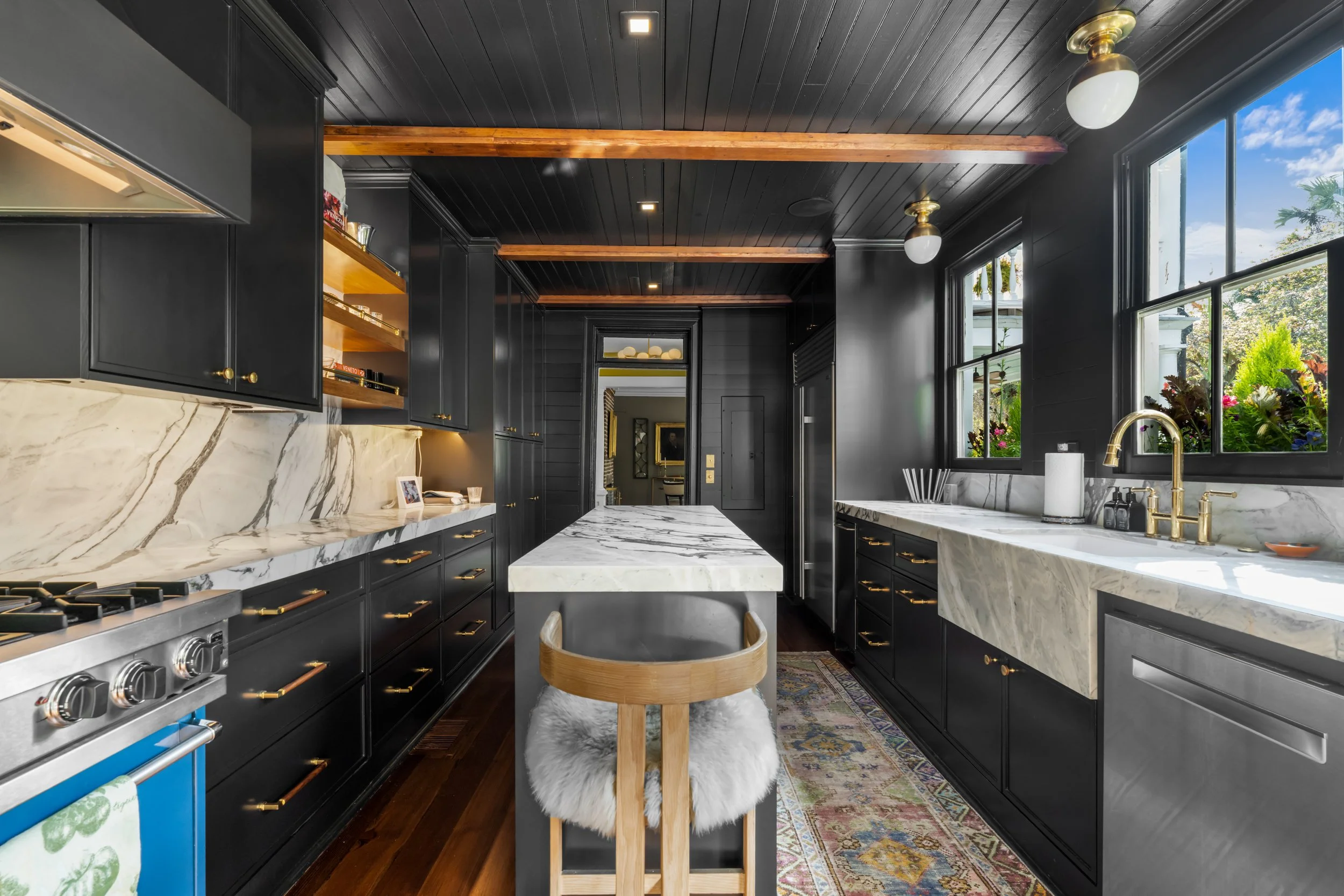 Modern kitchen with black cabinets, white marble countertops, and a marble farmhouse sink, illuminated by natural light through large windows.