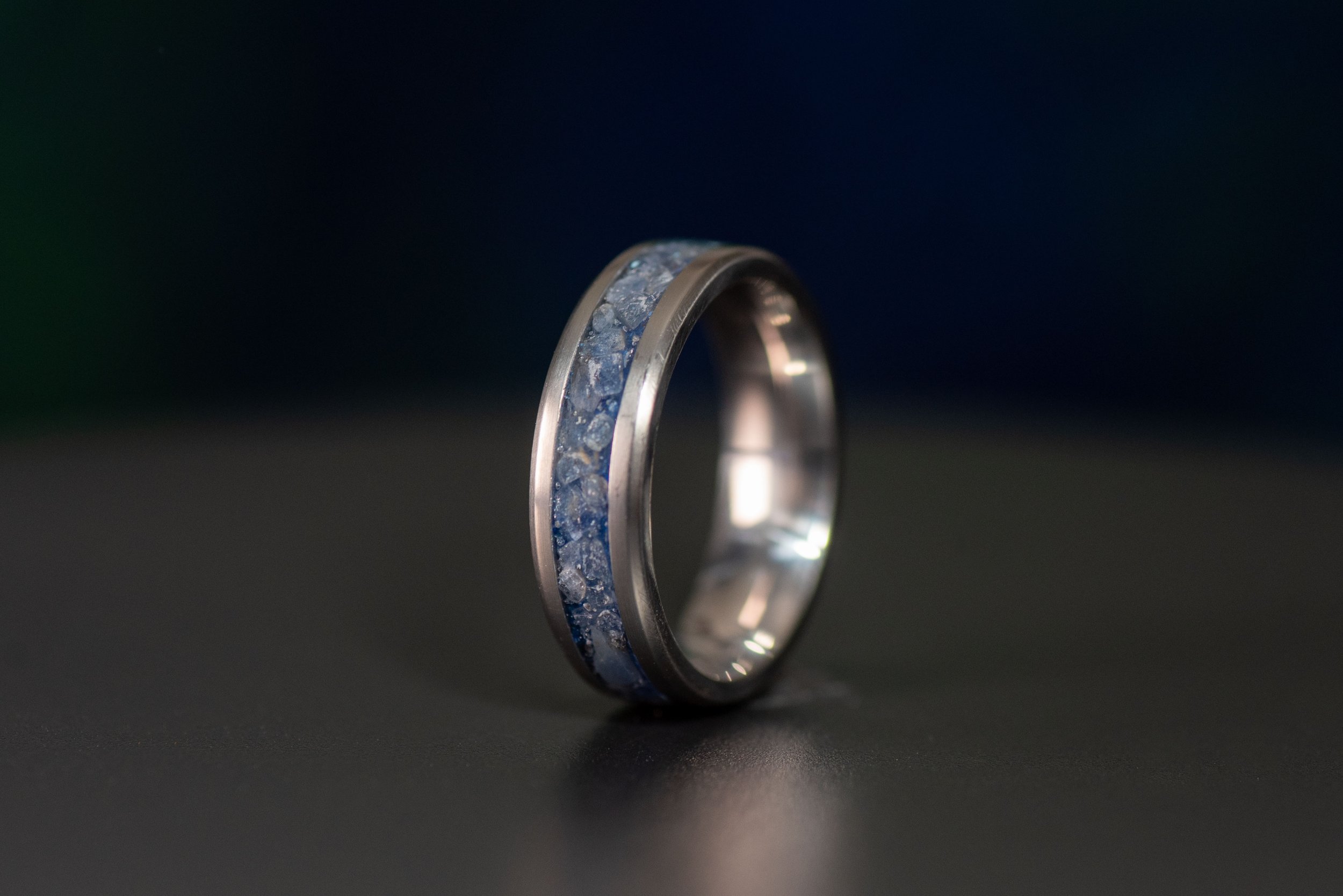 Close-up of a polished titanium band featuring a brilliant sapphire inlay, designed for men and women.