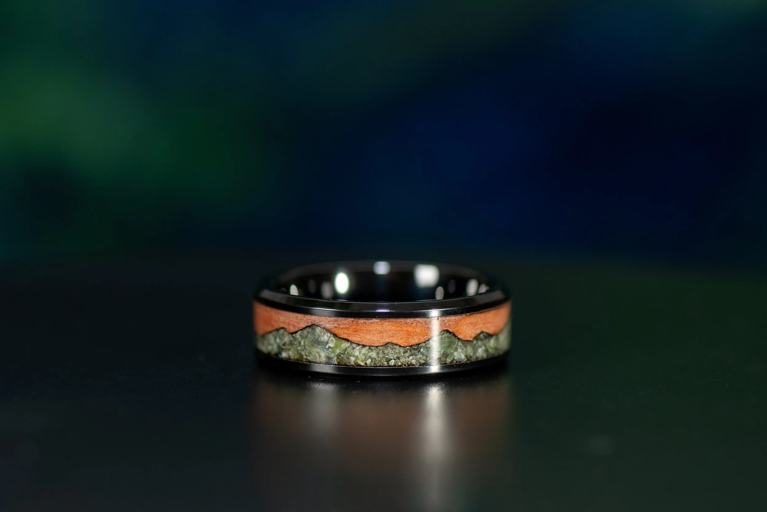 Black ceramic ring with tineo wood inlay and green jade mountain landscape design.