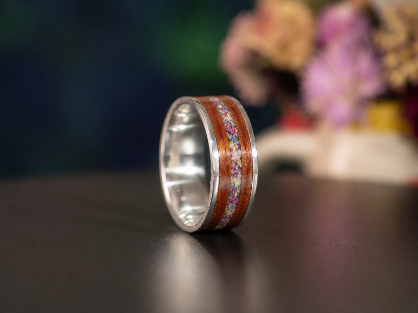 Side view of a handmade mahogany wood ring with a sterling silver core and preserved flower inlay through the center.