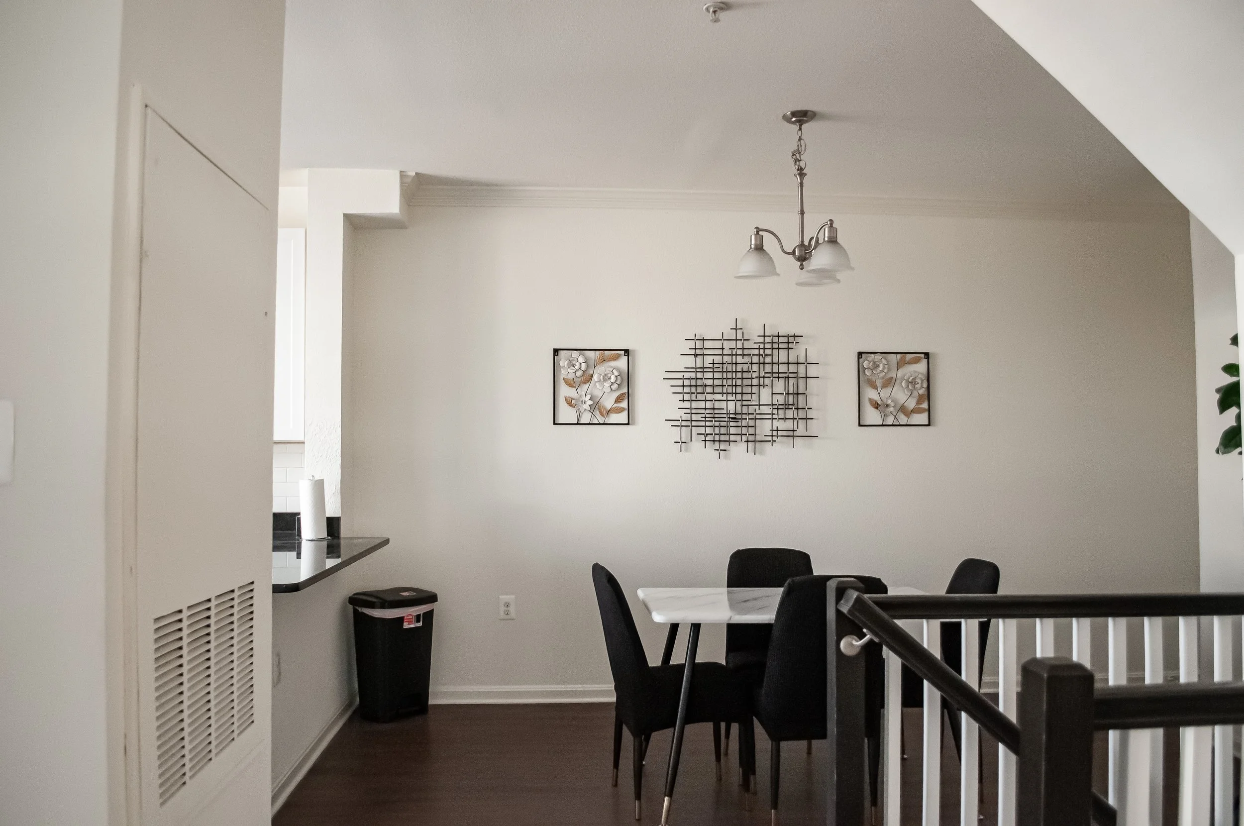 A dining room with a white table, black chairs, wall art, and a ceiling light fixture.