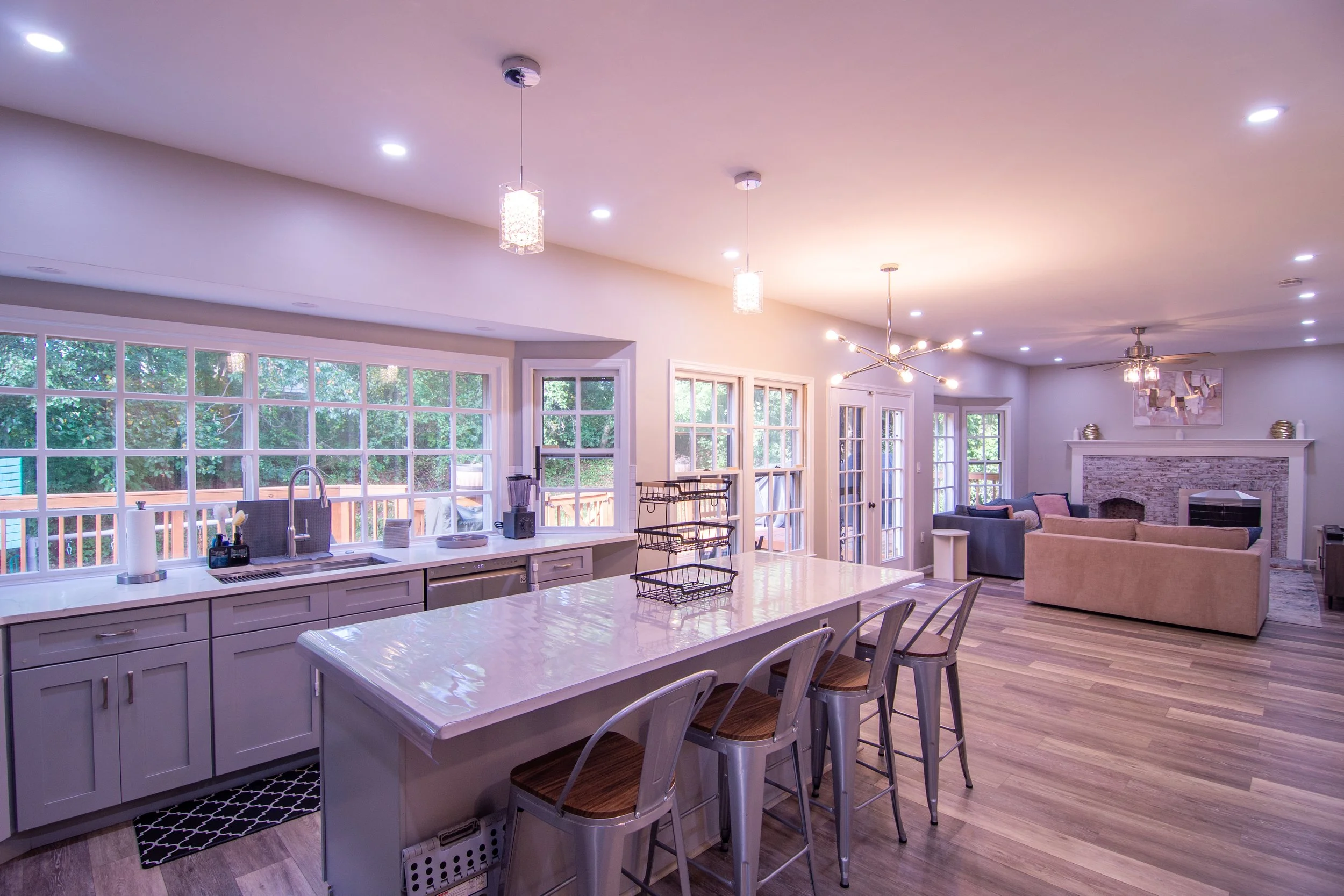 Open-concept kitchen and living room with large windows, pendant and ceiling lights, and modern decor.
