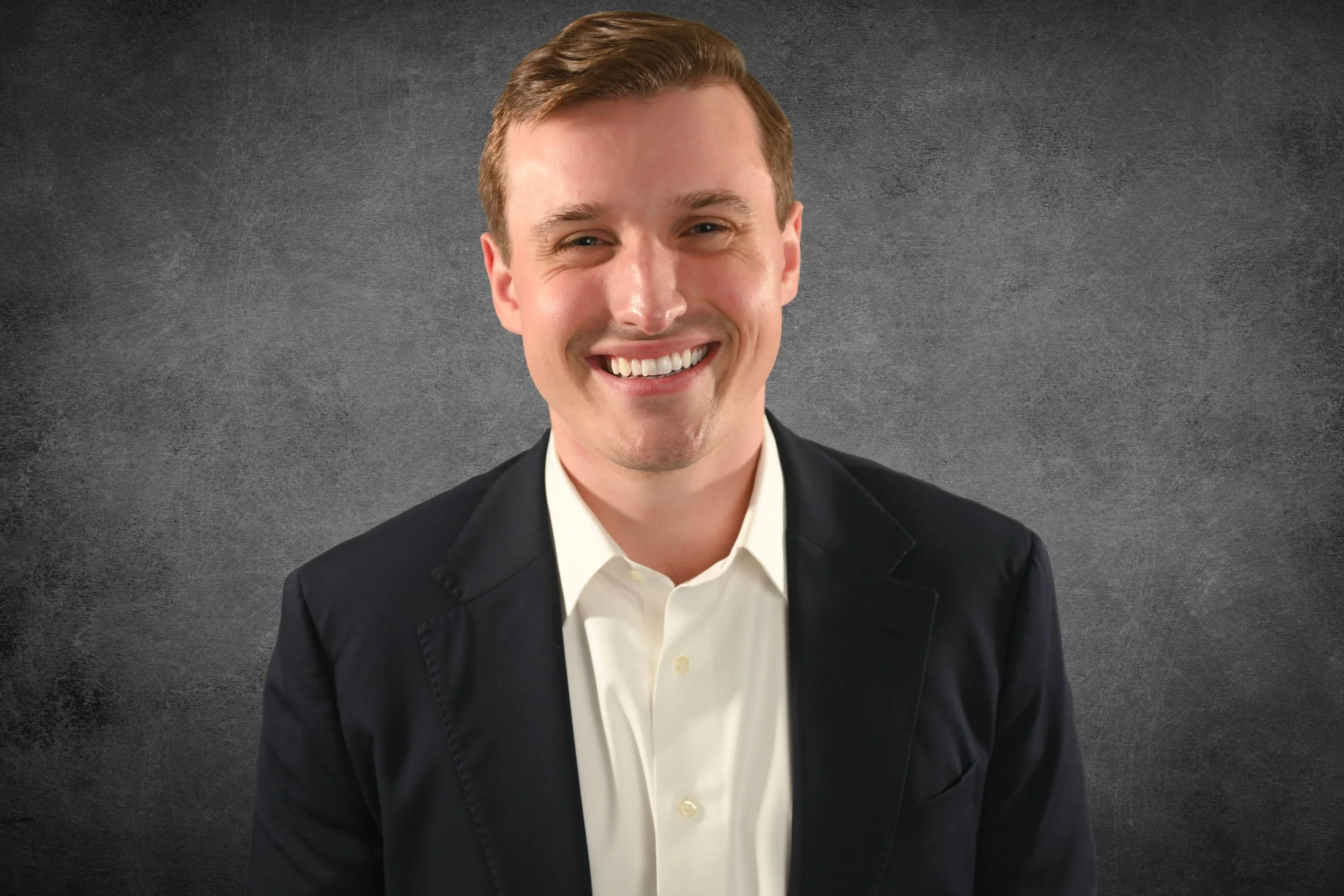 A smiling man in a suit and white shirt against a dark gray textured background.
