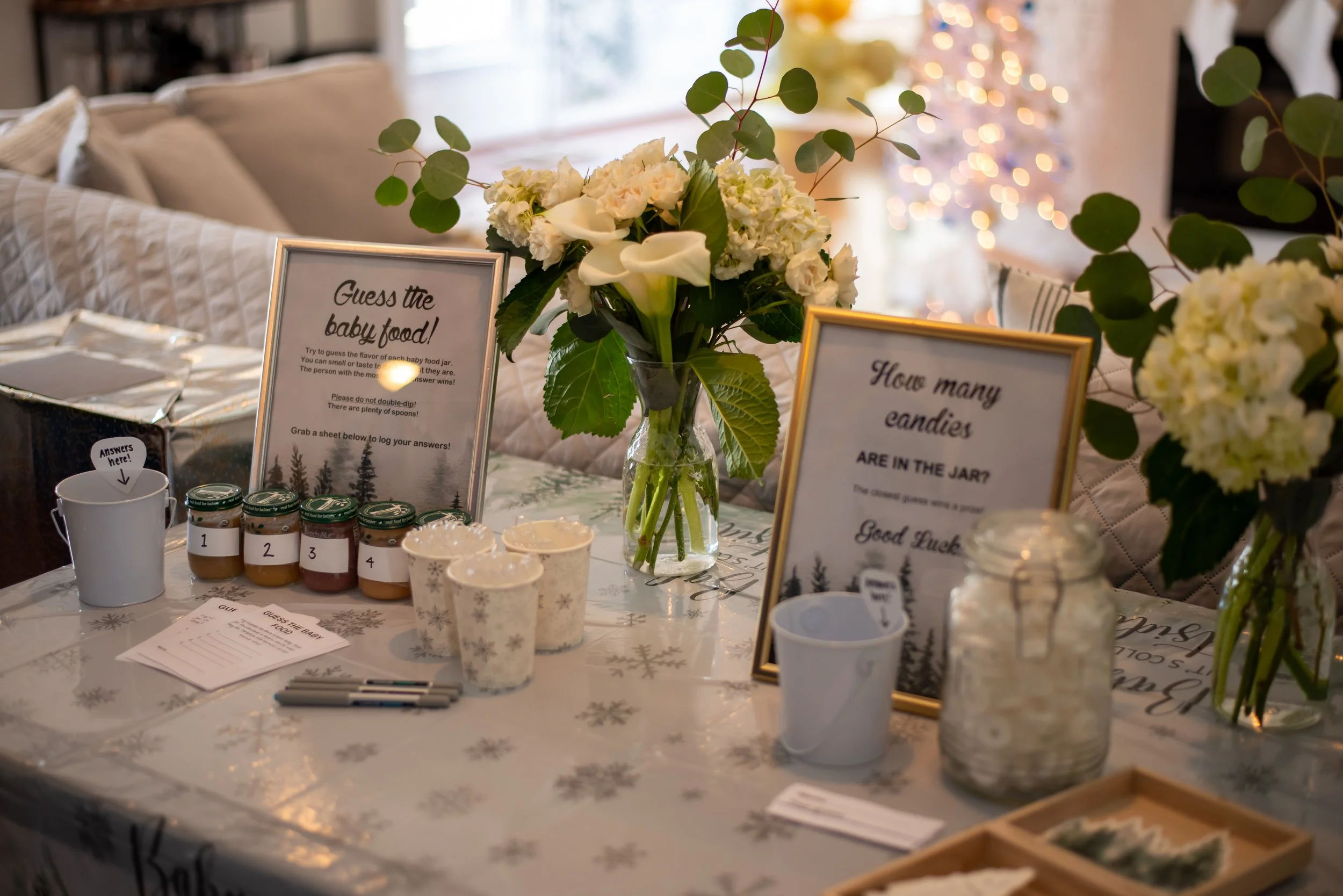 Table set up for a baby food guessing game with flowers, signs, jars of baby food, and markers.