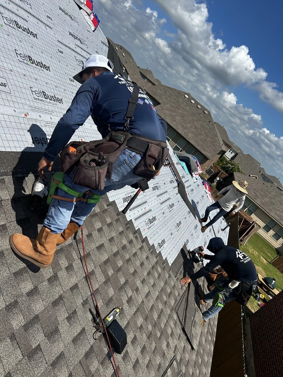 Roofing crew installing architectural asphalt shingles over synthetic underlayment during a roof replacement