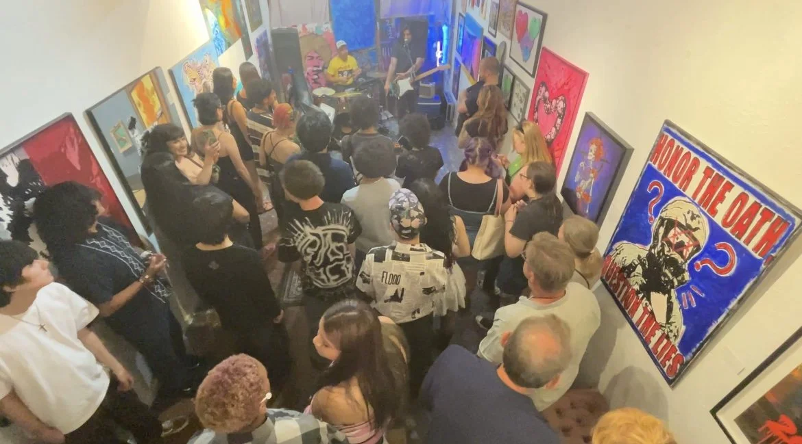 People gathered in an art gallery watching a live music performance with paintings on the walls