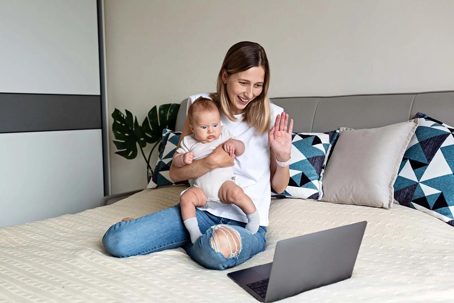 woman holding a baby and waving at her computer screen
