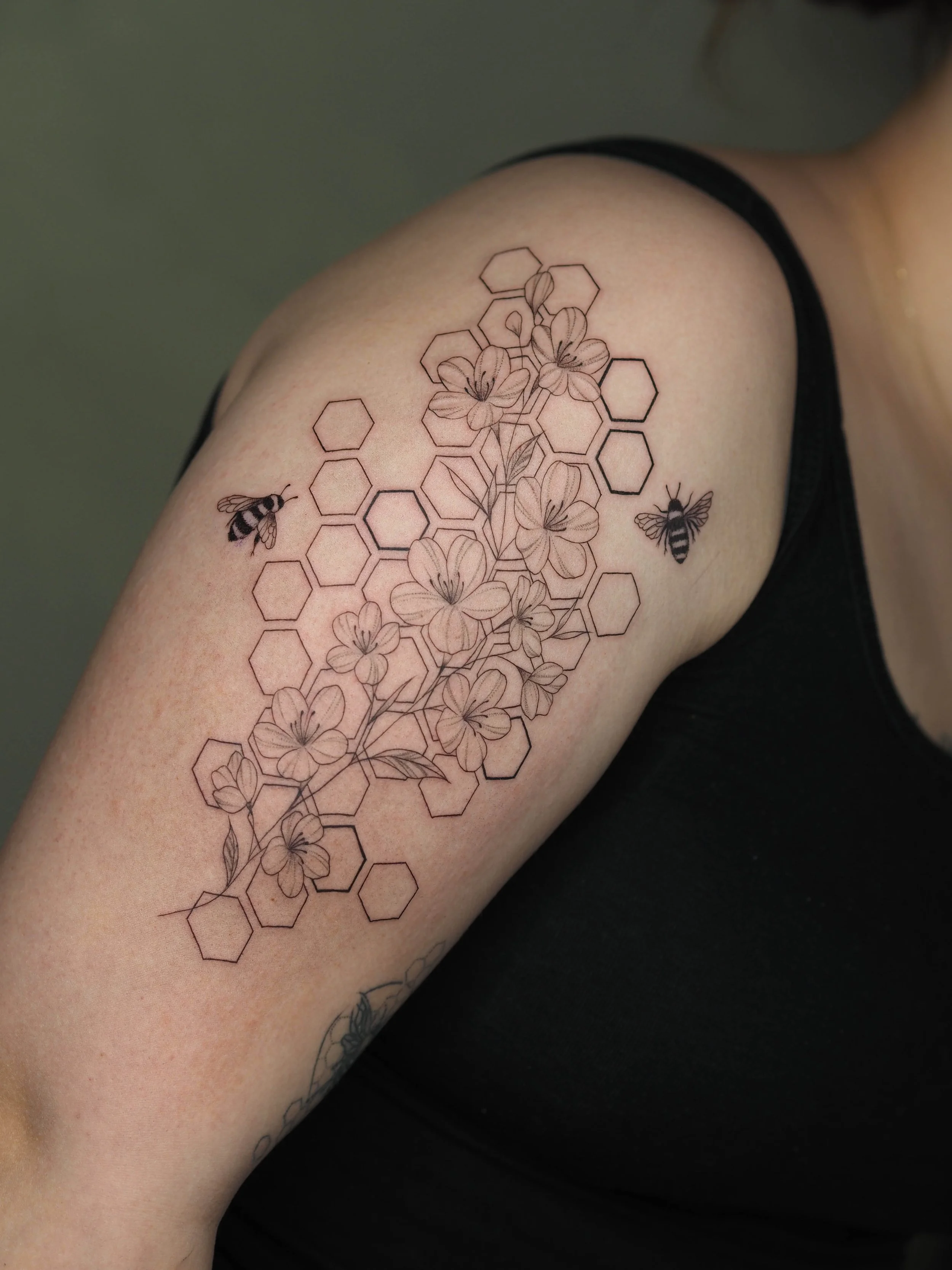 Tattoo auf dem Oberarm mit Bienen, Blumen und einem hexagonalen Muster