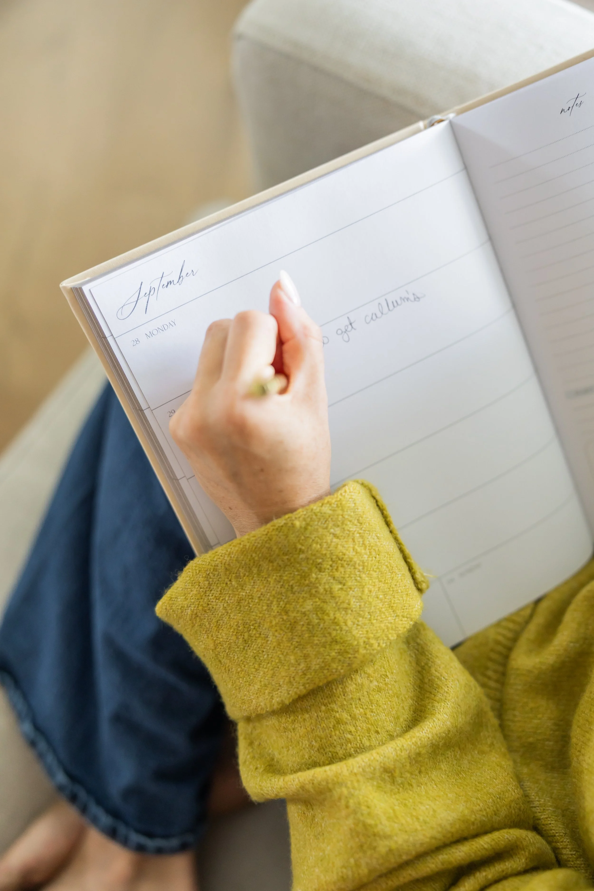 A person writing in a planner with a yellow sleeve, on their lap, with the date September 28 and notes about getting calluses.