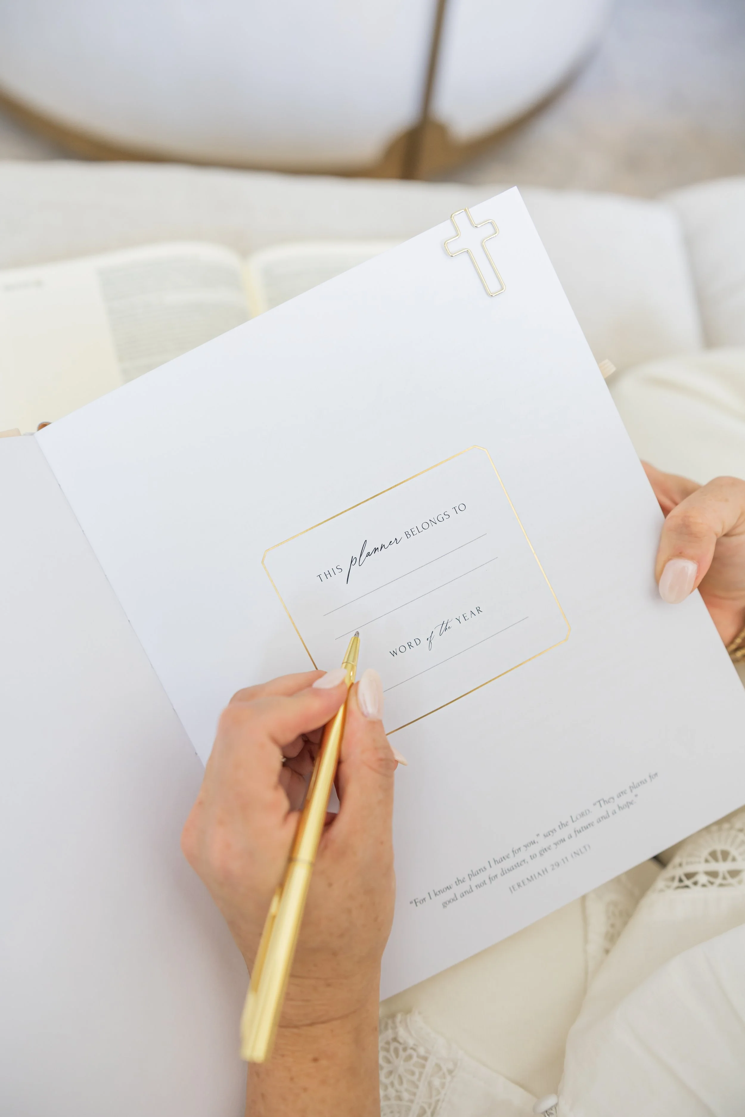 A person writing in a planner with a gold pen, with a cross paperclip attached at the top.
