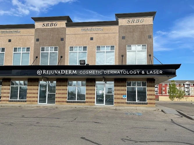 Front view of a skincare clinic named RejuvaDerm Cosmetic Dermatology & Laser, located on the ground floor of a beige brick building with the letters SRBG on the upper part, under a blue sky.
