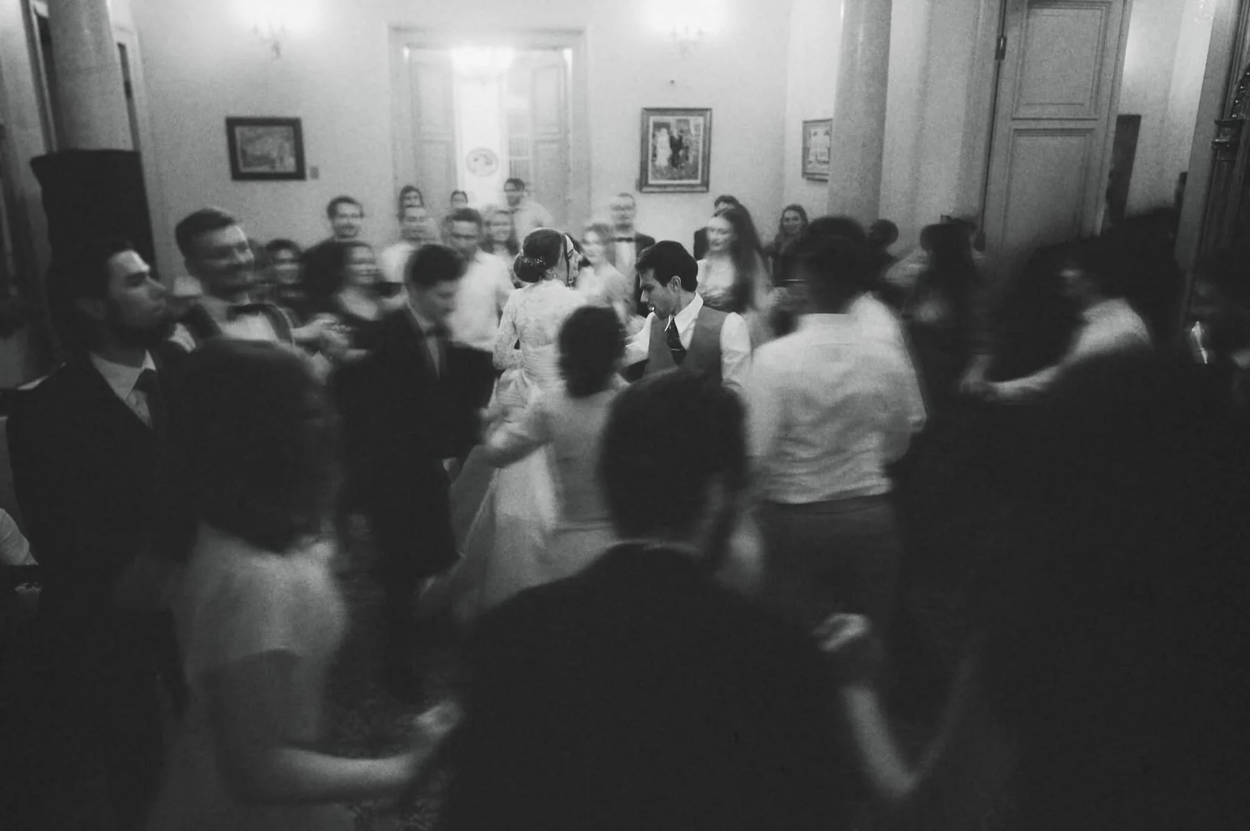 Miri dansând printre invitați, surprinși în mișcare într-o fotografie de nuntă alb-negru.