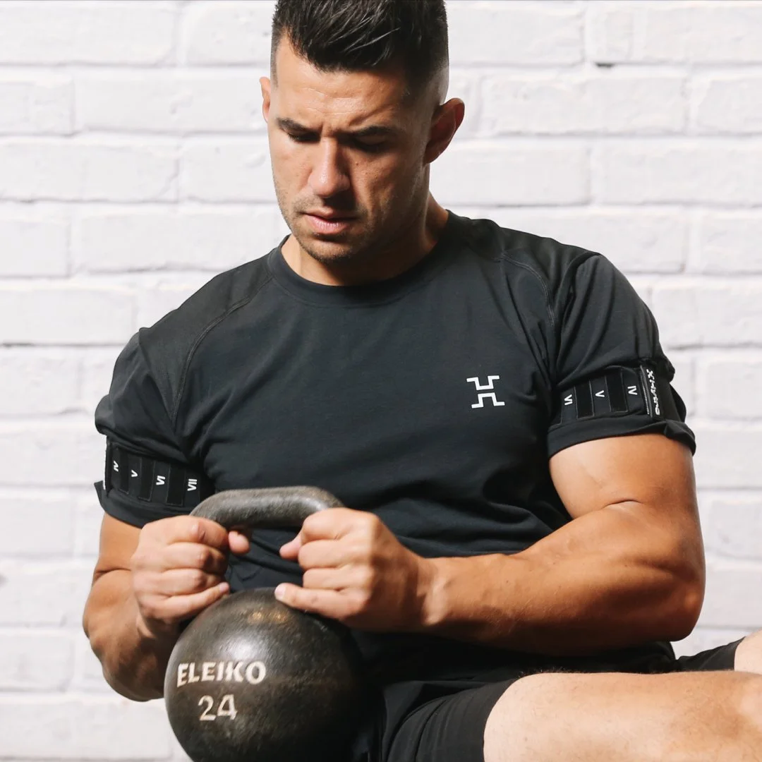 Man in black athletic shirt lifting a kettlebell in front of a white brick wall