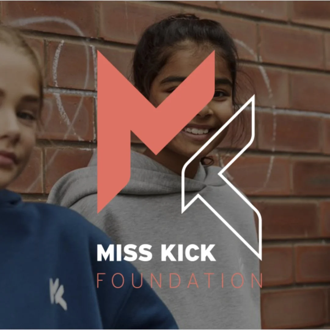 Two smiling girls standing against a brick wall, with a logo of a large stylized 'K' and the text 'Miss Kick Foundation' overlaid.