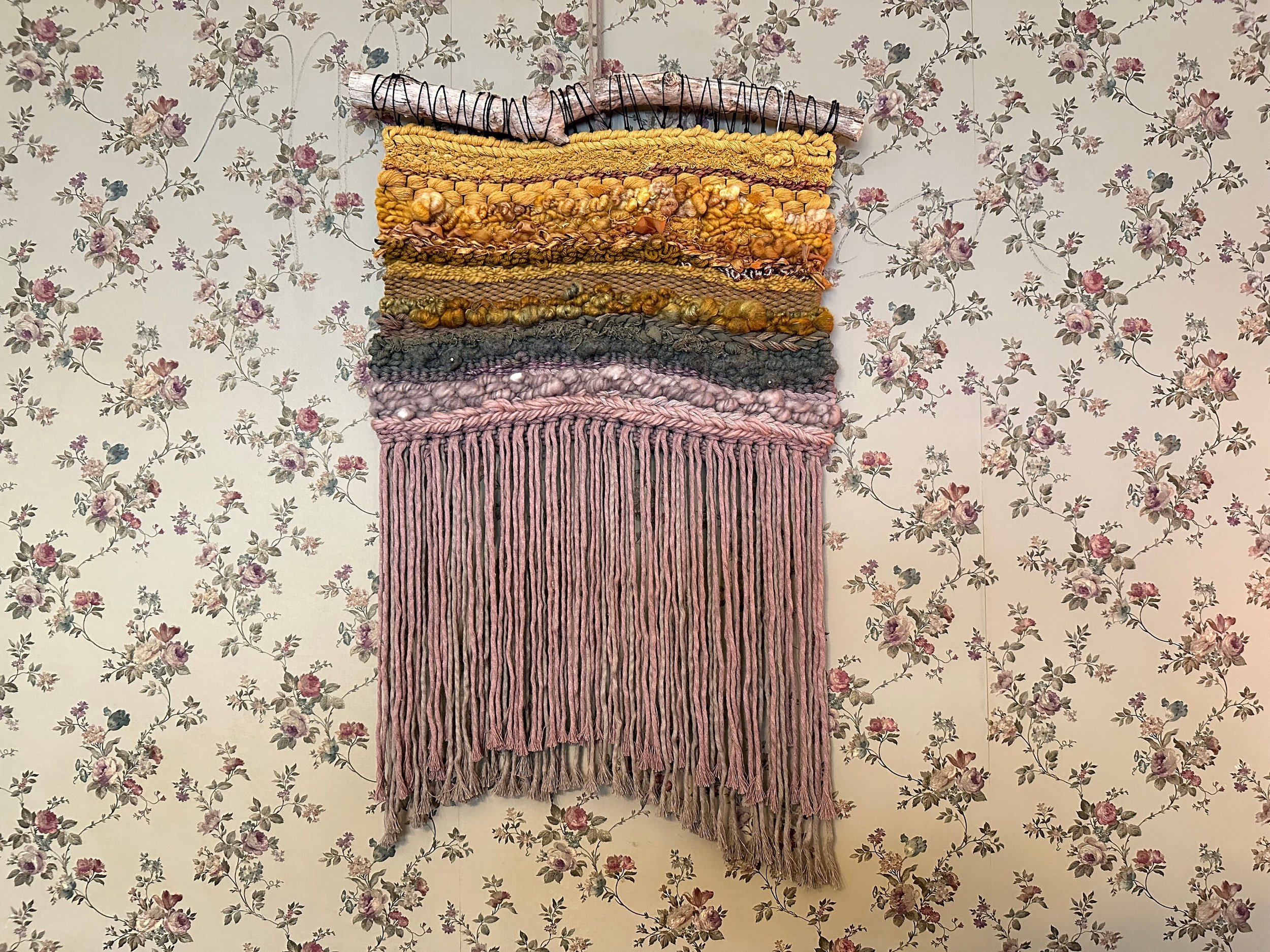 handmade woven tapestry in golds, greens, taupes and mauves hangs on a driftwood