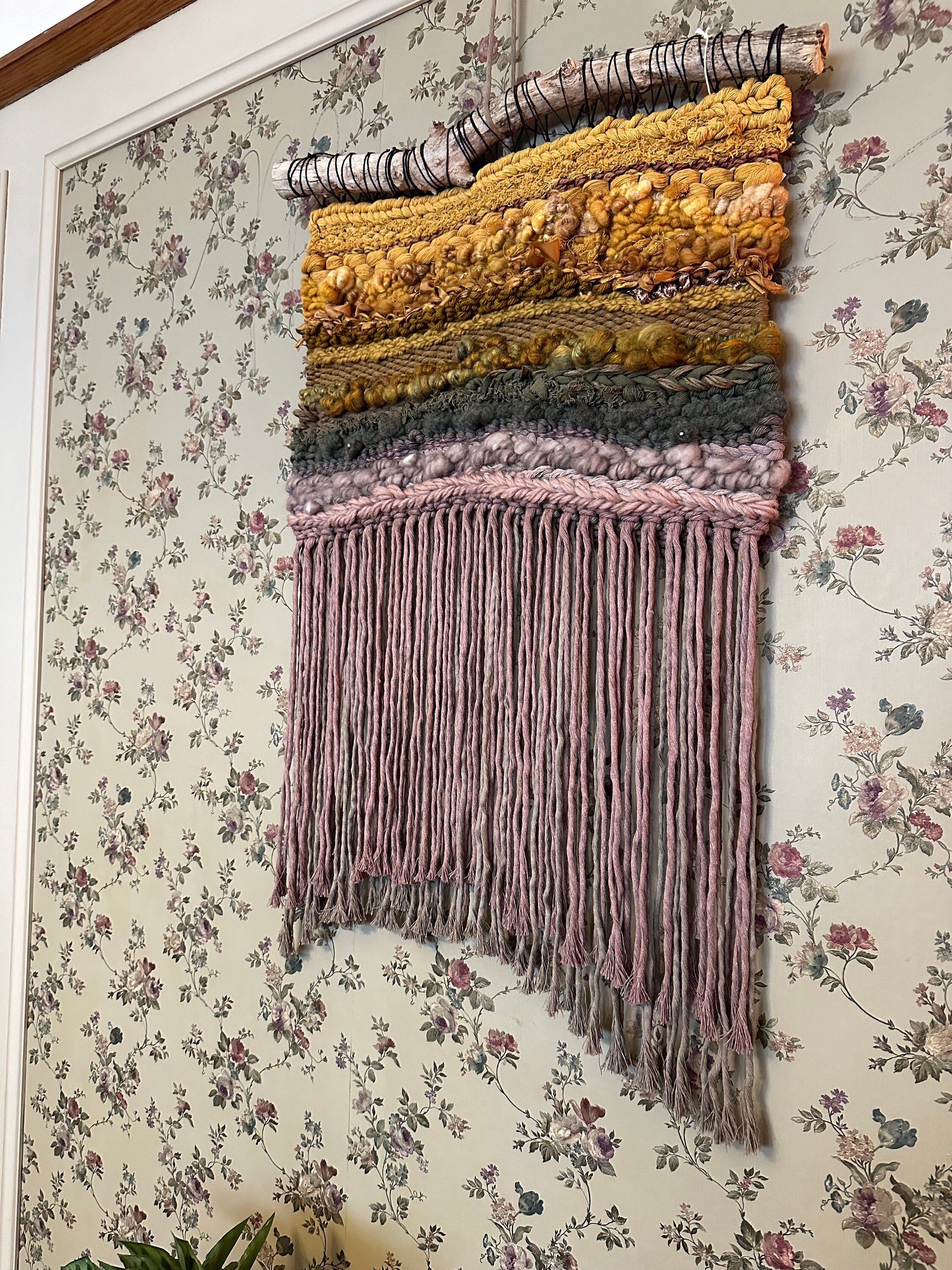 handmade woven tapestry in golds, greens, taupes and mauves hangs on a driftwood