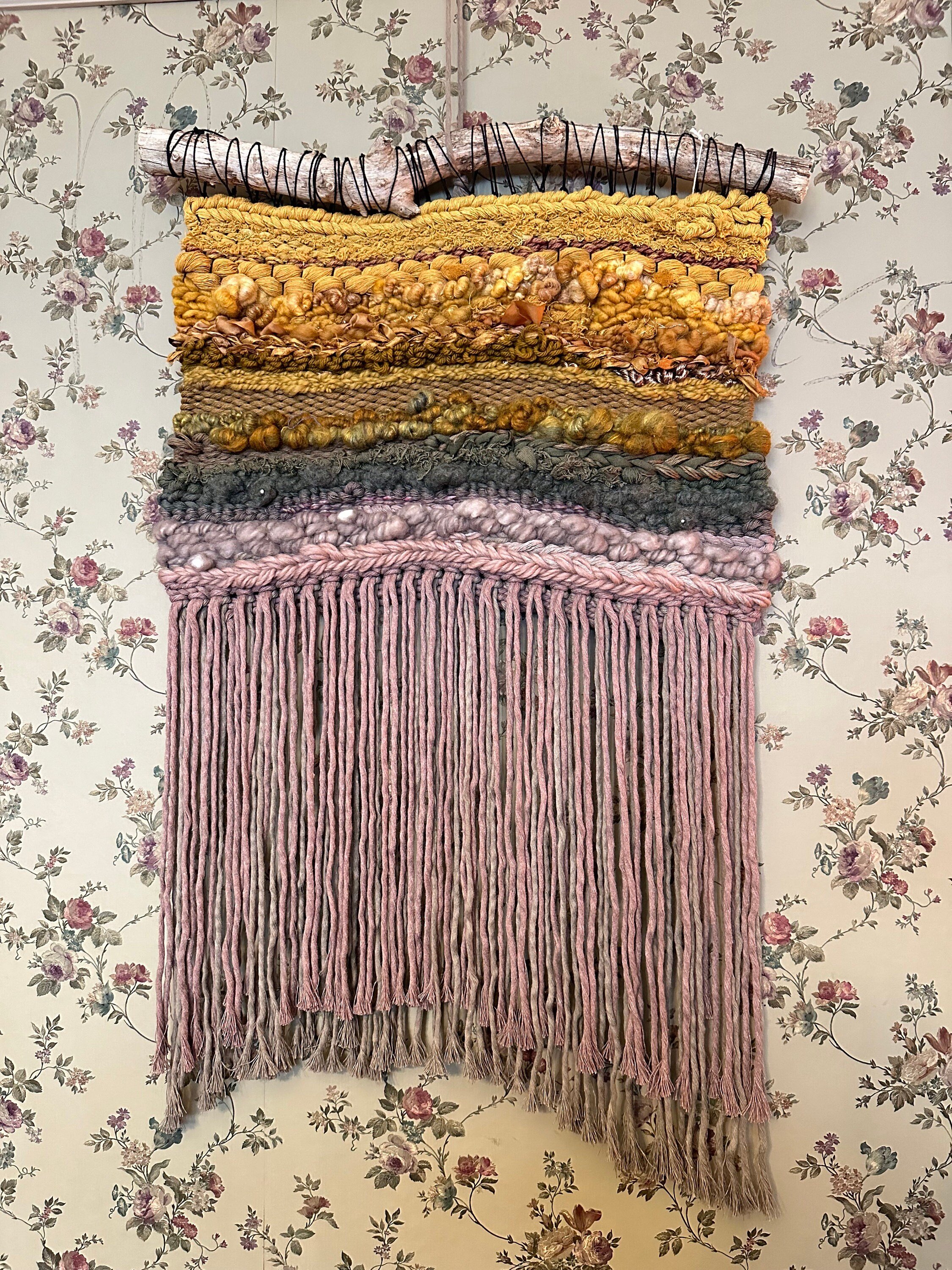 handmade woven tapestry in golds, greens, taupes and mauves hangs on a driftwood