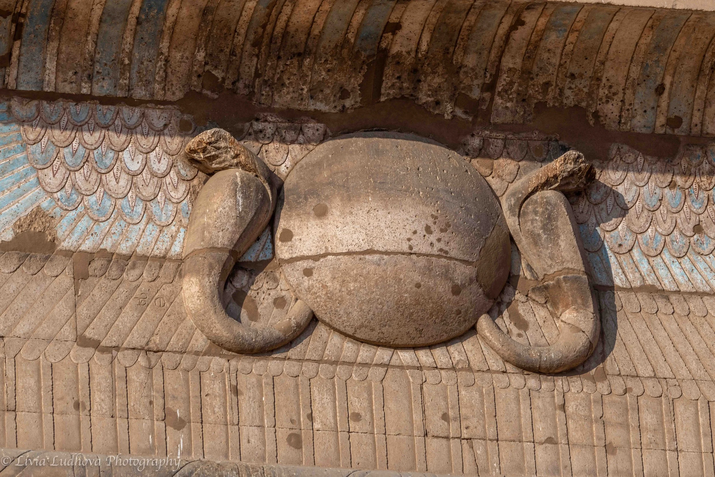 Above the pylon gate of the Temple of Horus, the winged sun disk spreads its protective wings—an emblem of Horus and divine kingship, symbolizing protection, cosmic order, and the triumph of light over chaos as one enters the sacred space.