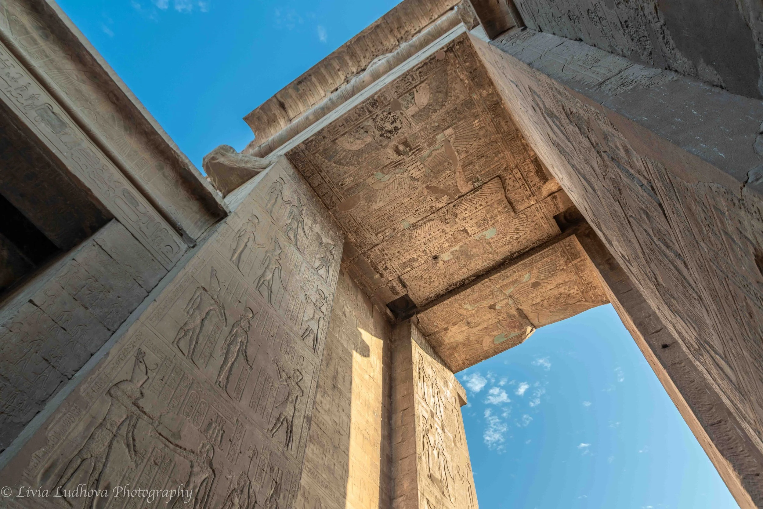 Looking up through the monumental gateway of the Temple of Horus, where carved sandstone walls rise like a stone canyon toward the open sky.