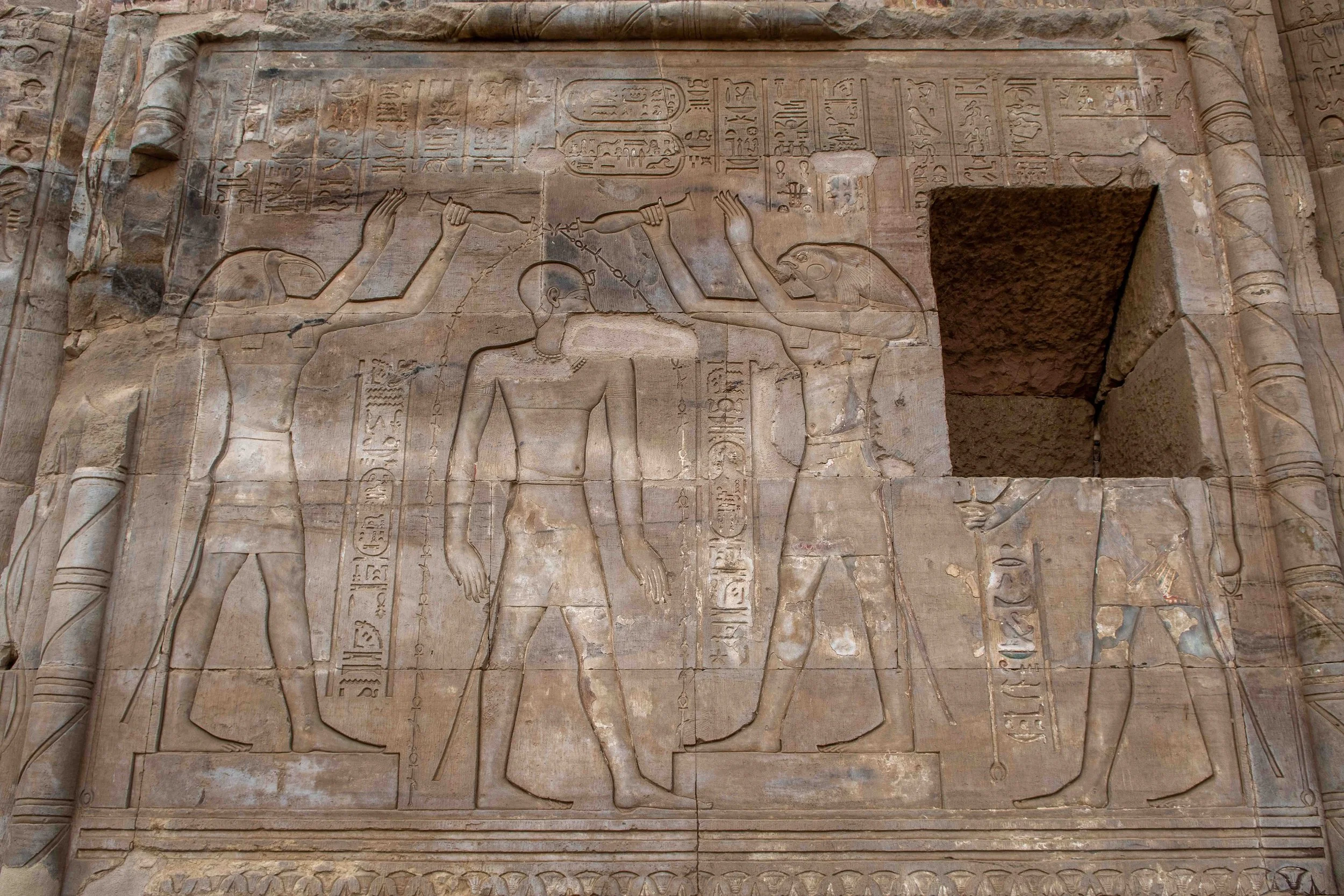 The king presents between two deities - Thoth, the ibis-headed god of wisdom and writing, and Horus, the falcon-headed god of kingship.