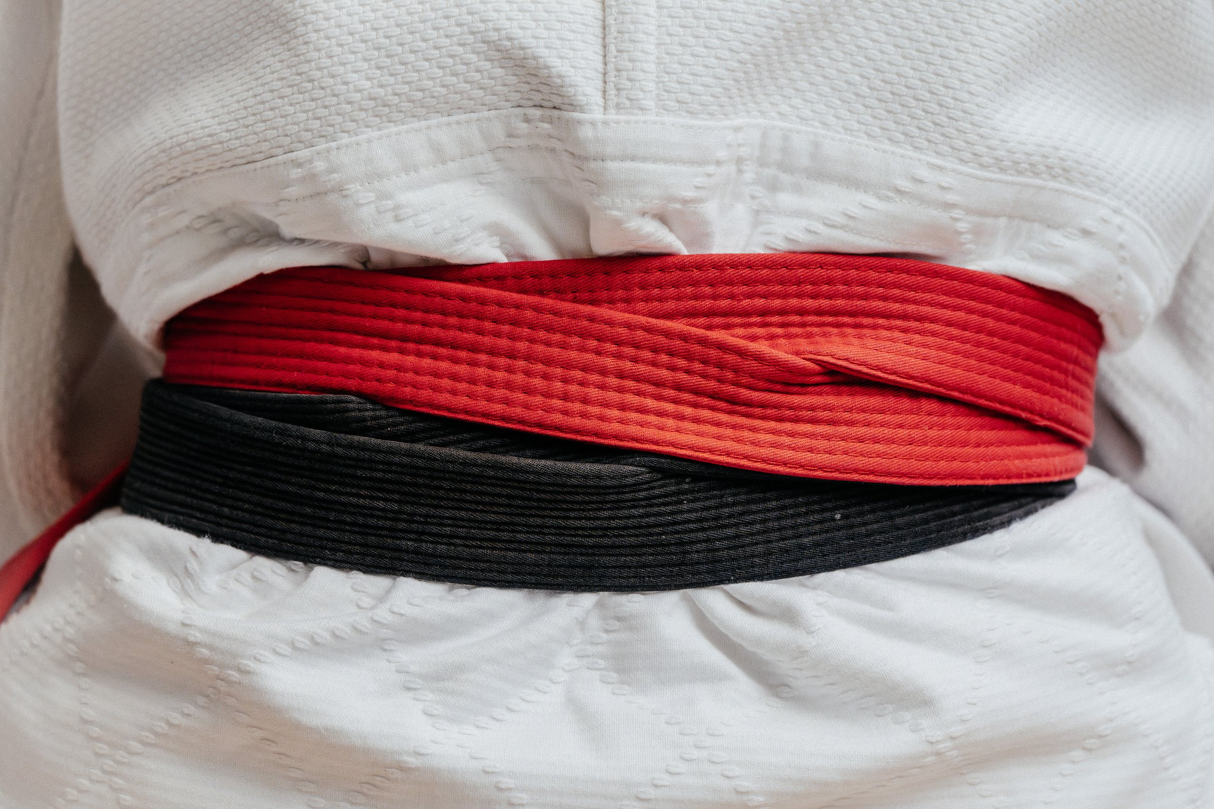 Drei Gürtel in Rot, Schwarz und Rot auf einer weißen Gi