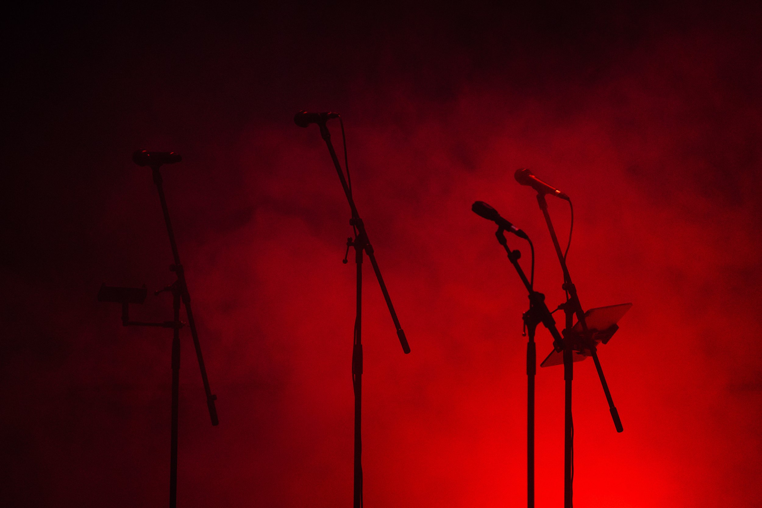 Mehrere Mikrofone auf Ständern vor rotem, nebligem Bühnenhintergrund.