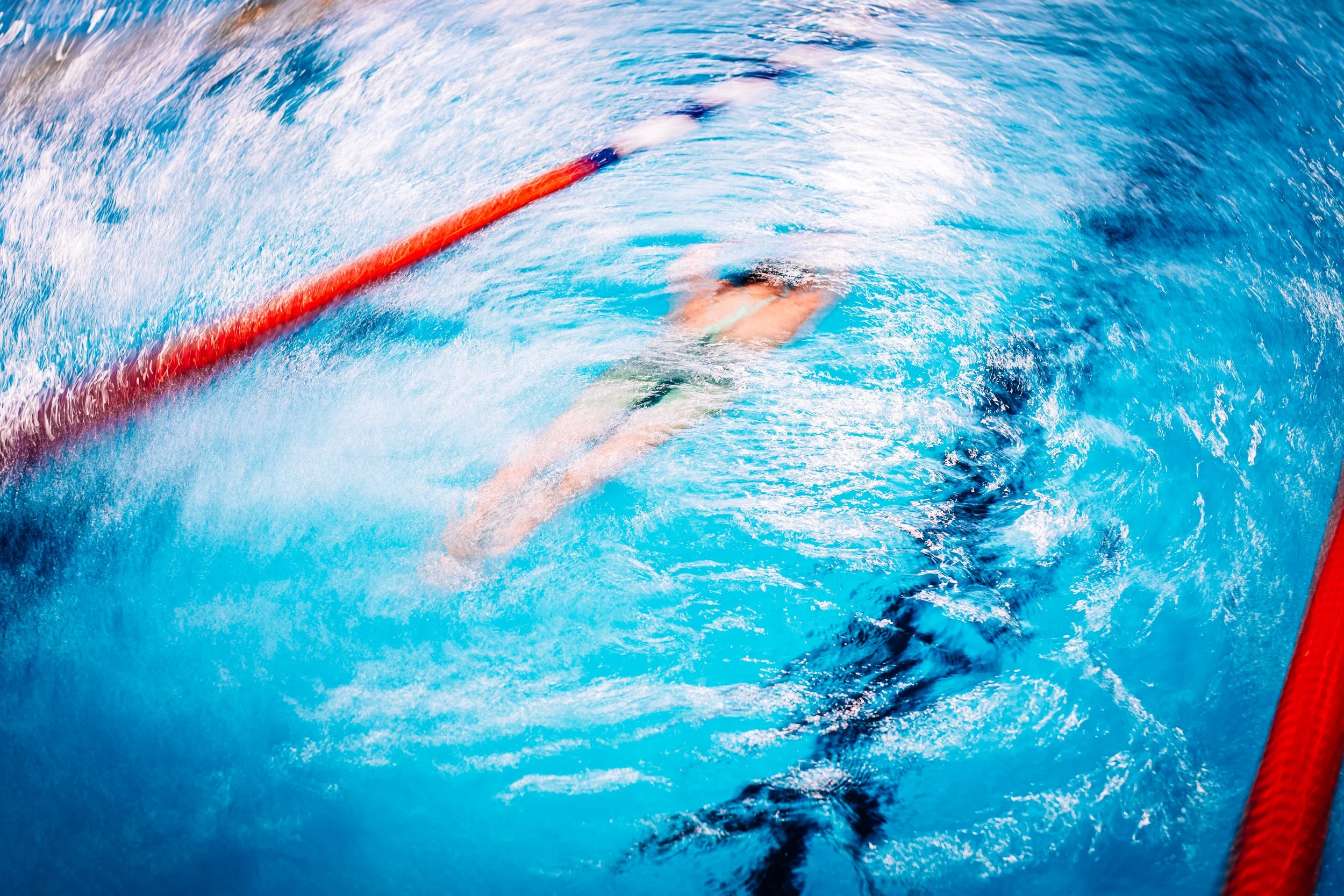 Ein Schwimmer taucht im Wasser während eines Wettkampfs in einer Schwimmhalle, mit roten Trennlinien im Wasser.