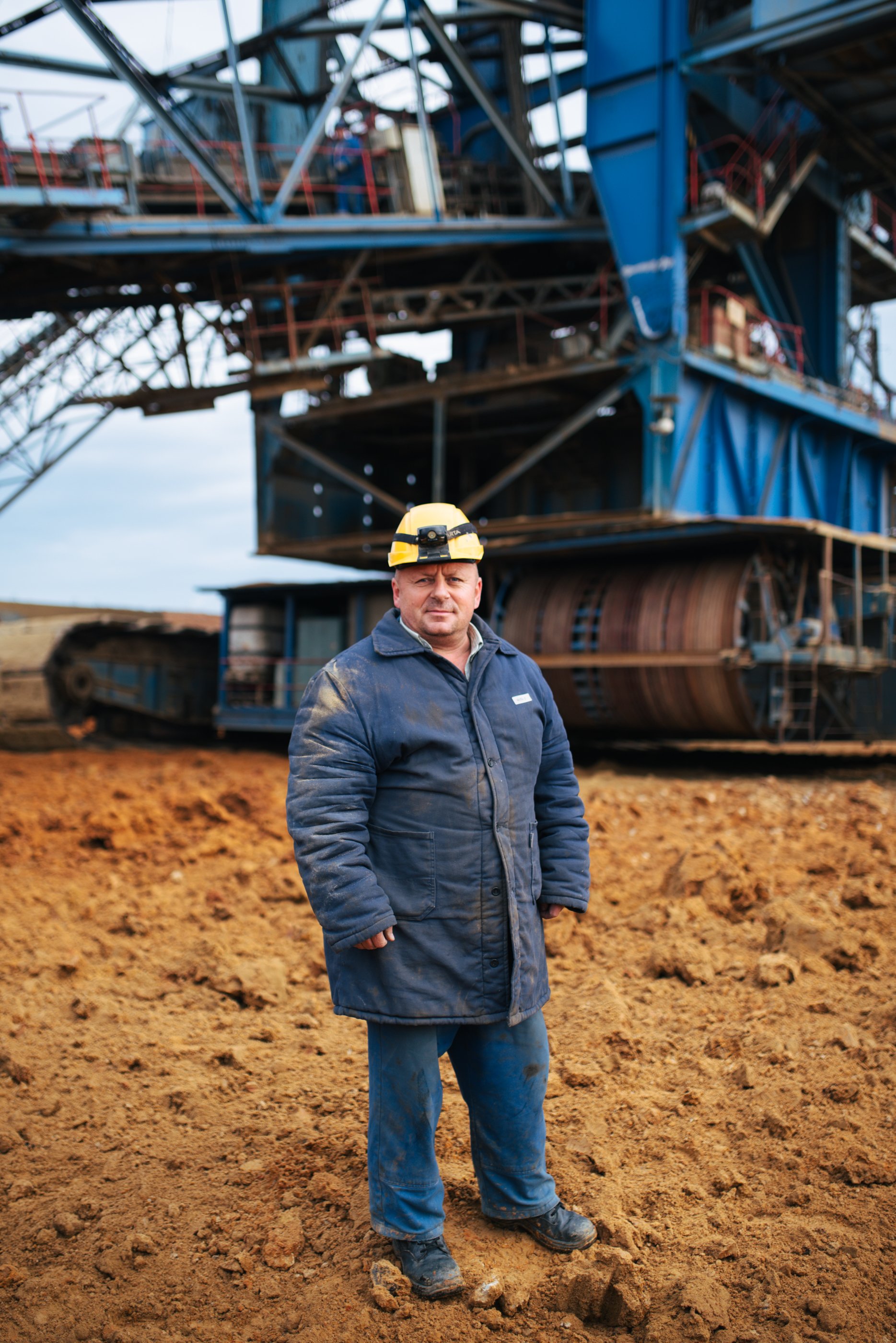Arbeiter in Schutzkleidung und Helm auf einer Baustelle mit großer Maschinenkonstruktion im Hintergrund.