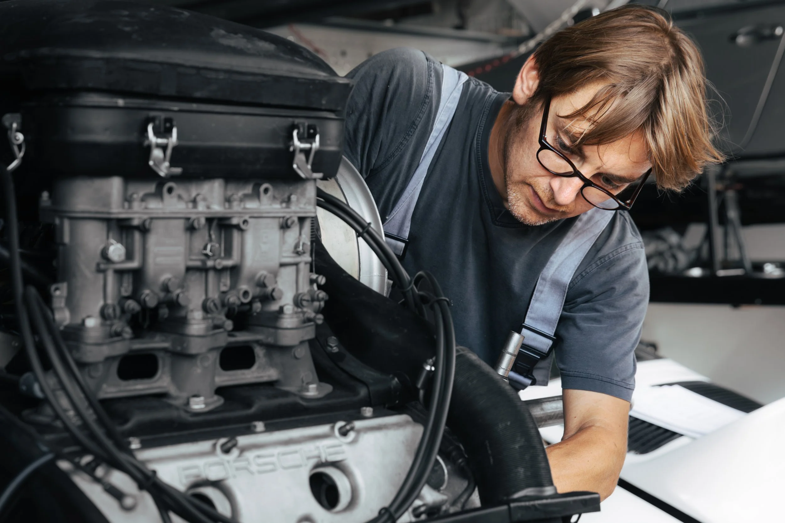 Ein Mann mit Brille arbeitet an einem Auto-Motor in einer Werkstatt.