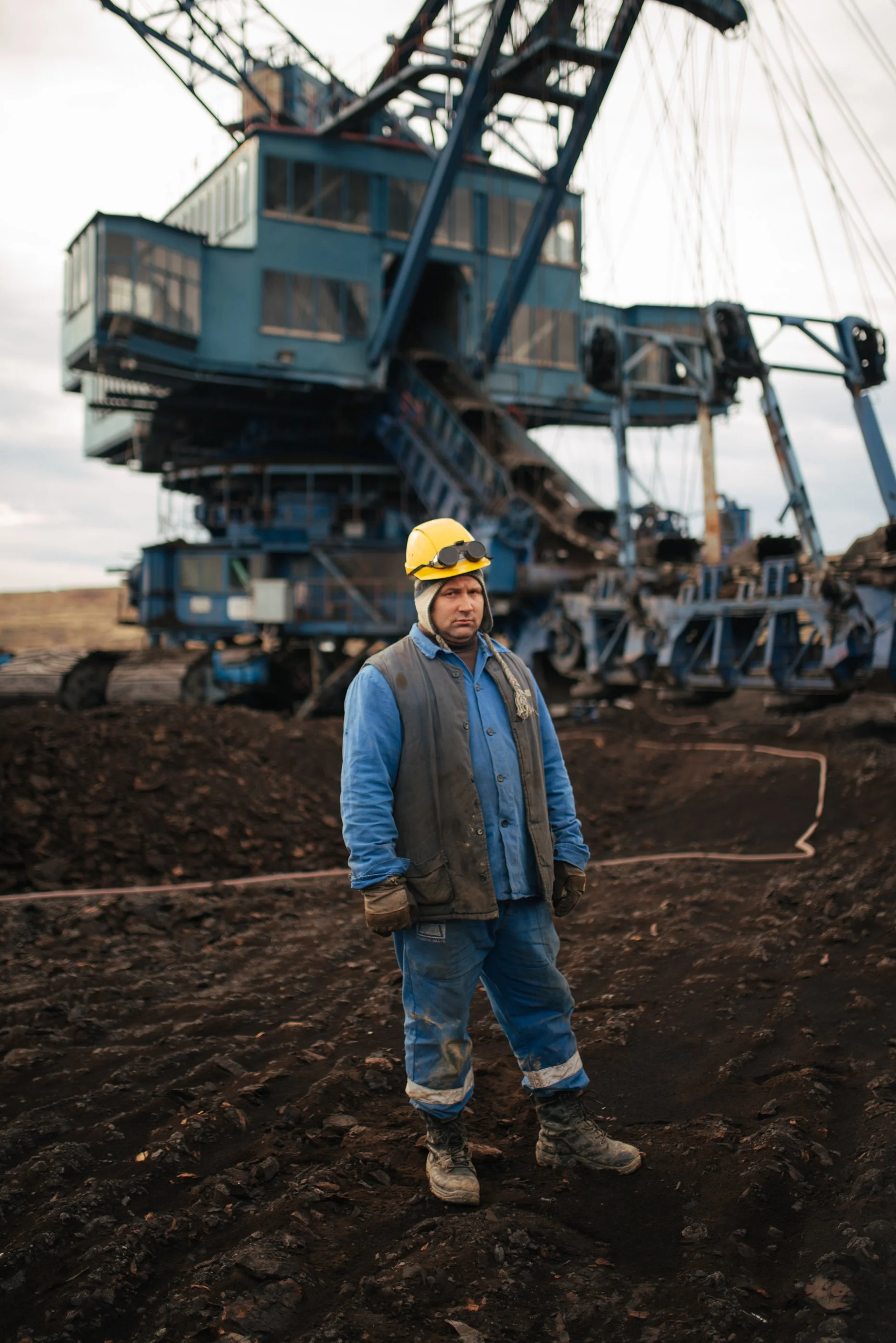 Ein Arbeiter steht vor einer riesigen Bohranlage auf einer Ölförderplattform, trägt Schutzhelm, Handschuhe und Arbeitskleidung.