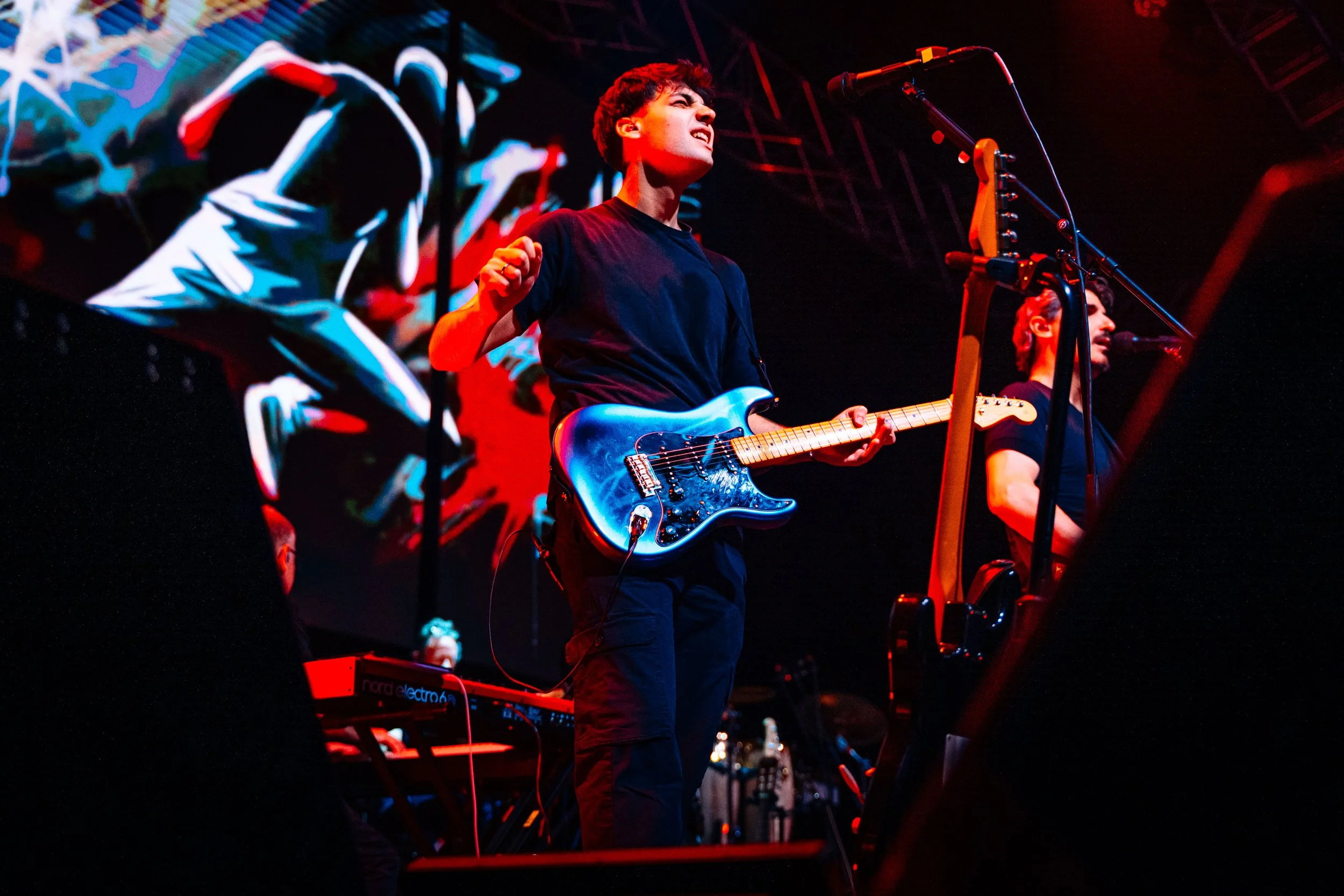 Musiker spielt Gitarre auf Bühne bei einem Live-Konzert, mit roten und blauen Lichteffekten im Hintergrund.