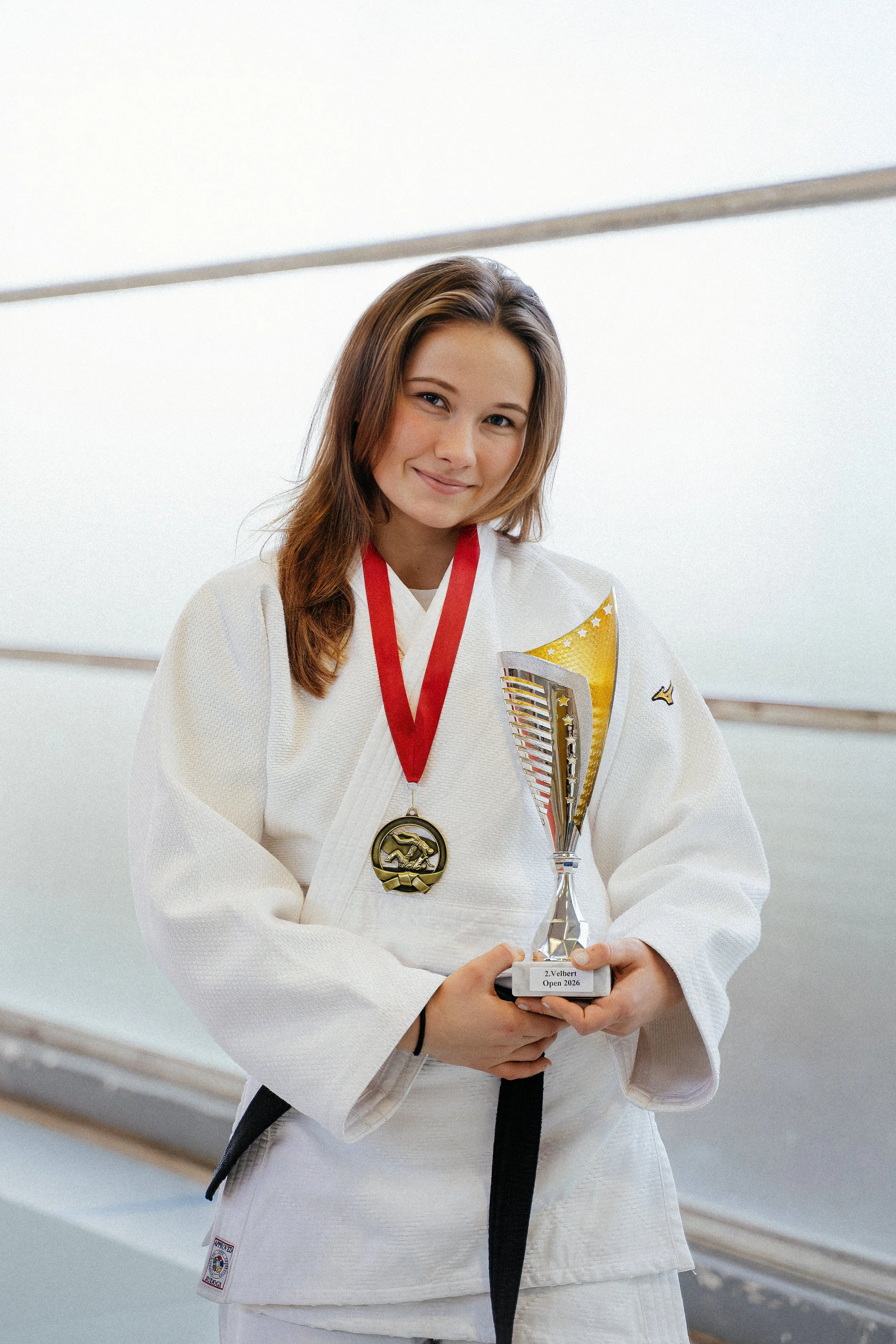 Junge Frau in Judo-Gi mit Medaille und Pokal nach Wettkampf
