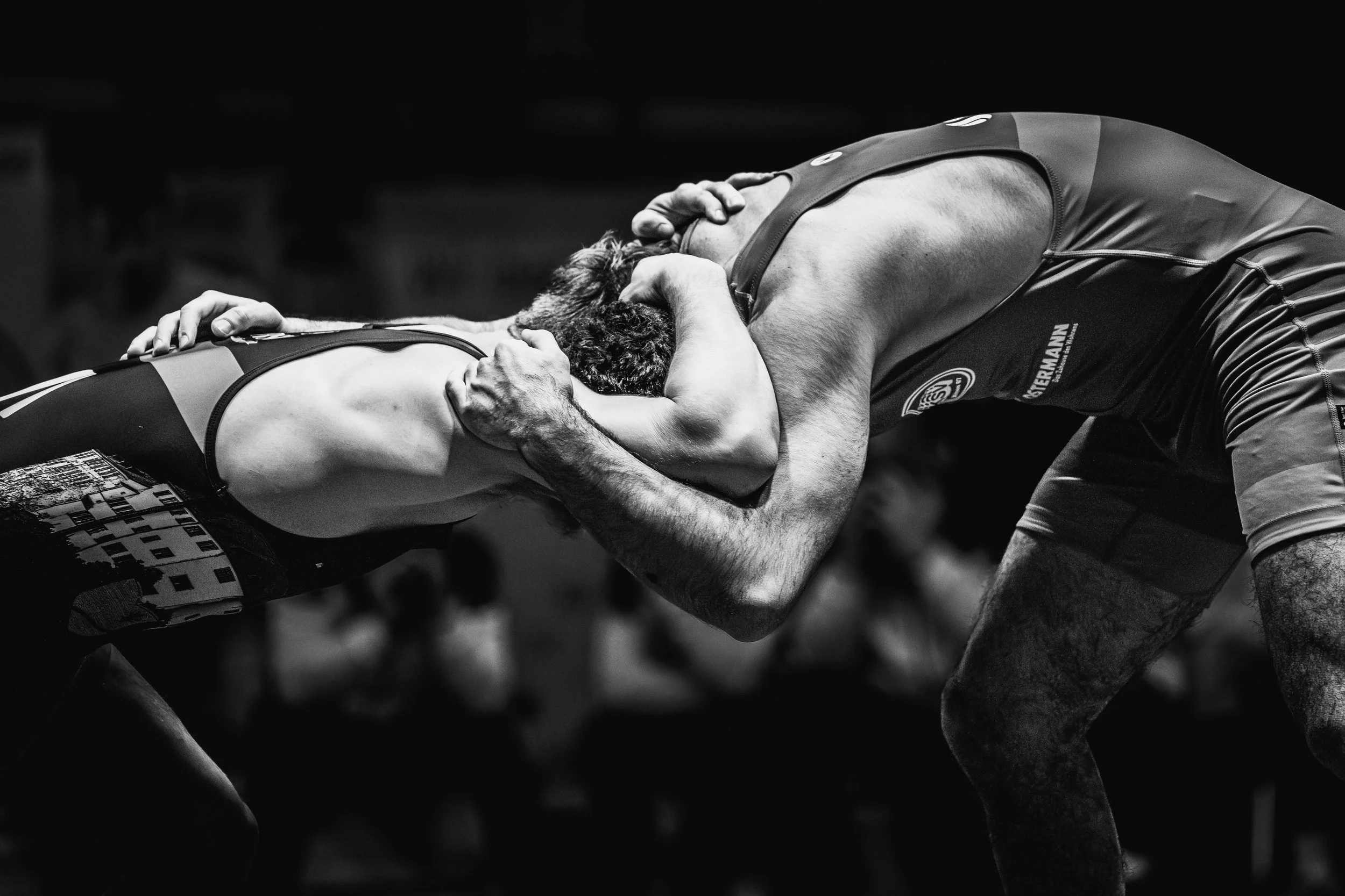 Zwei Ringer im Kopf an Kopf, die in einem Wrestling-Wettkampf gegeneinander antreten, mit einem Fokus auf ihre Anstrengung und Kraft in einer Schwarz-Weiß-Aufnahme.