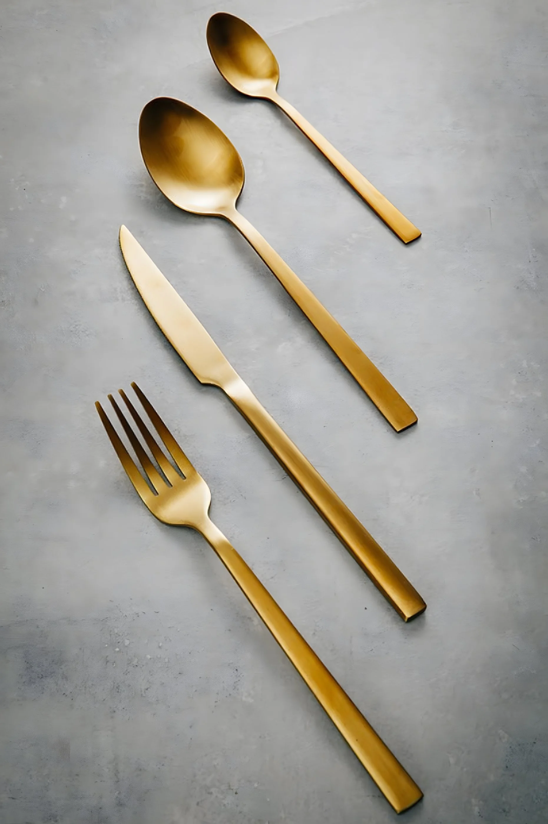 Goldene Bestecksets, bestehend aus einem Löffel, einem Messer und einer Gabel, auf grauem Hintergrund