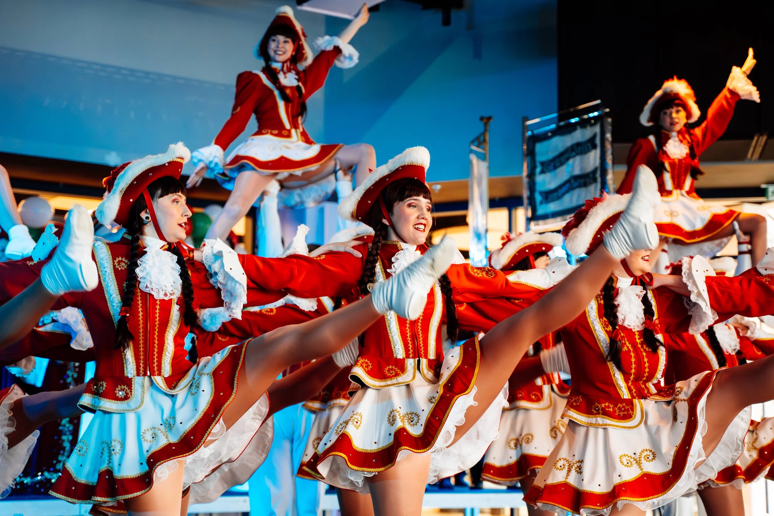 Tänzerinnen in rot-weißer Karnevals- oder Faschingskostüm während einer Show, performing im Stil eines militärischen Marsch, mit einem gleichzeitigen High-Kick auf einer Bühne.