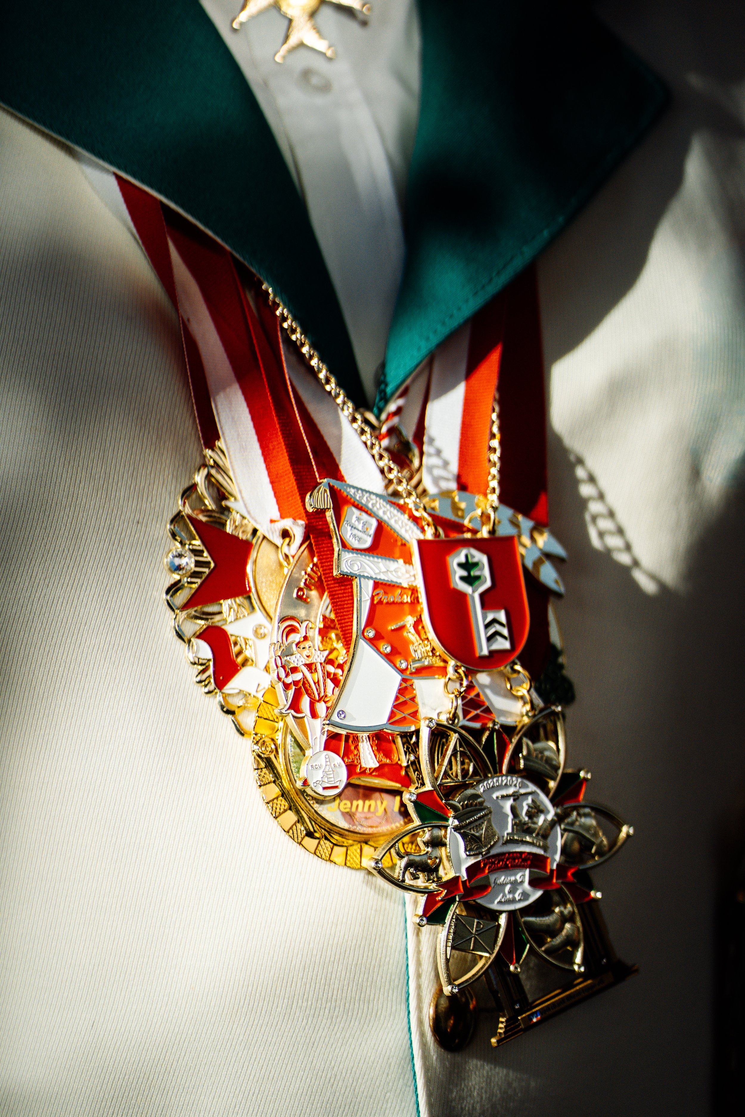 Nahaufnahme von mehreren Orden, die an einer Person mit weißem Jackett mit grüner Umrandung getragen werden.