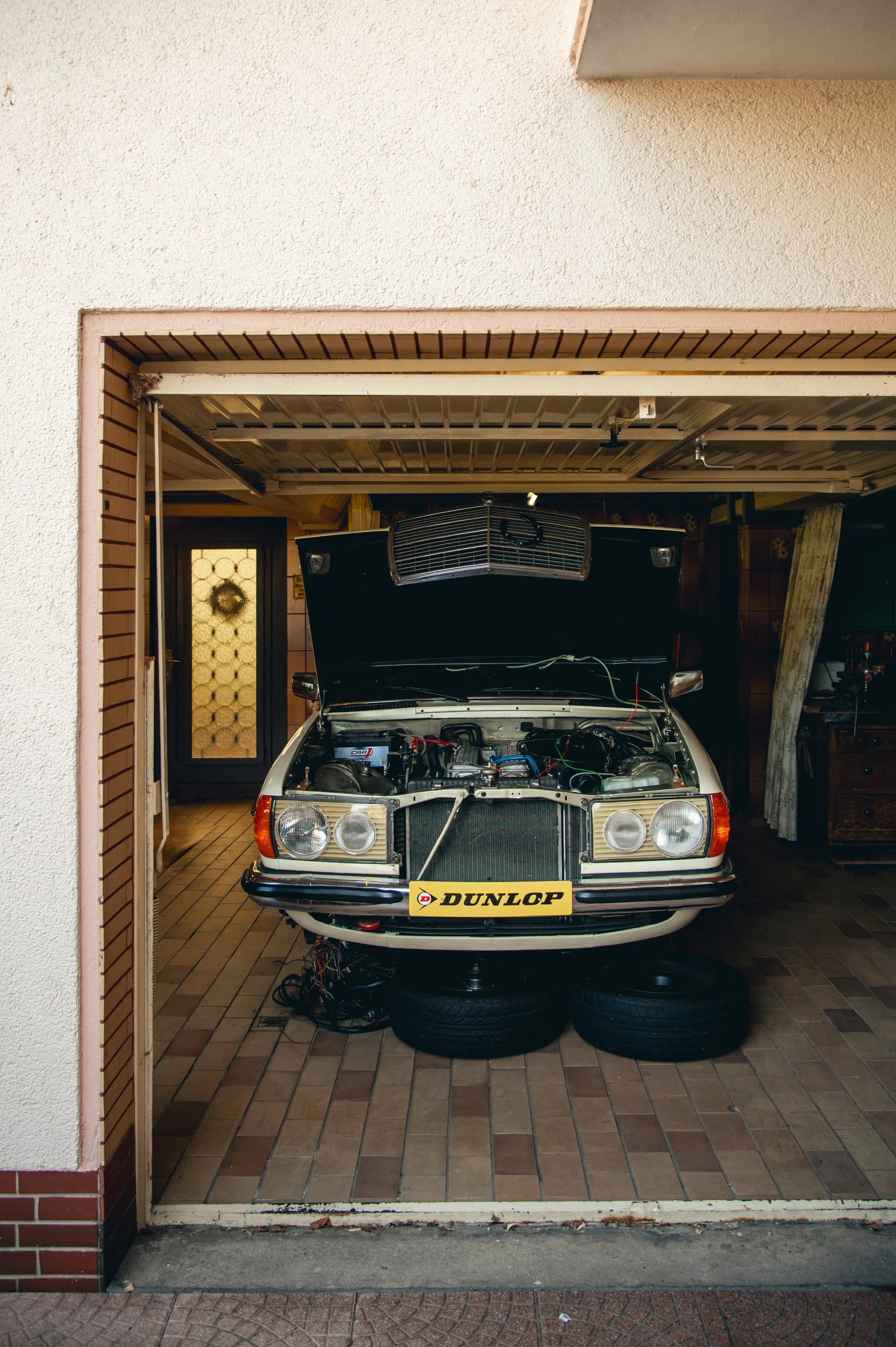 Klassischer weißer Auto mit offenem Motorhaube in Garage, auf vier Reifen, mit Dunlop-Nummernschild, im Innenraum.