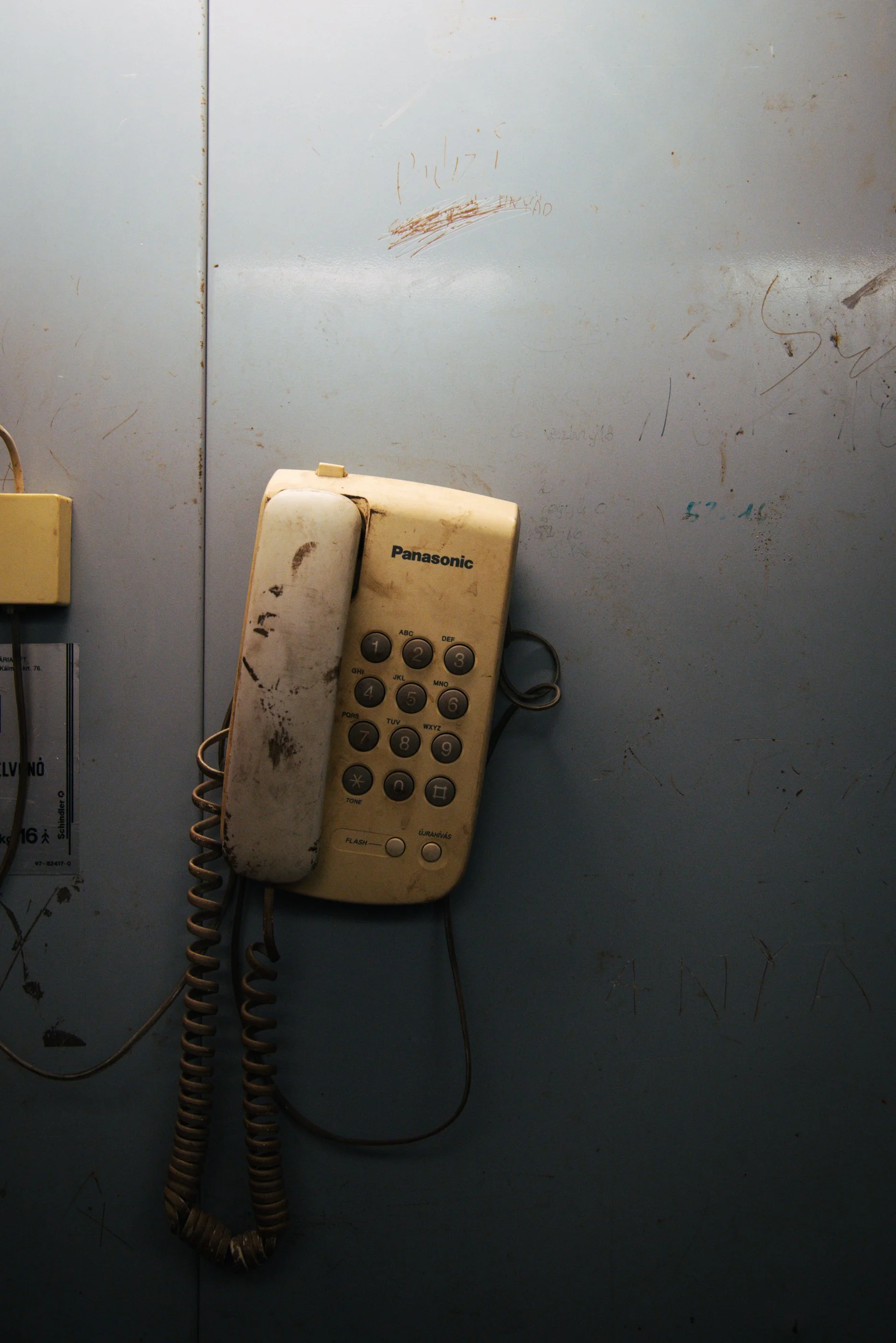 Ein alter, schmutziger Festnetztelefon an einer grauen Wand mit Rostflecken und Kratzern.
