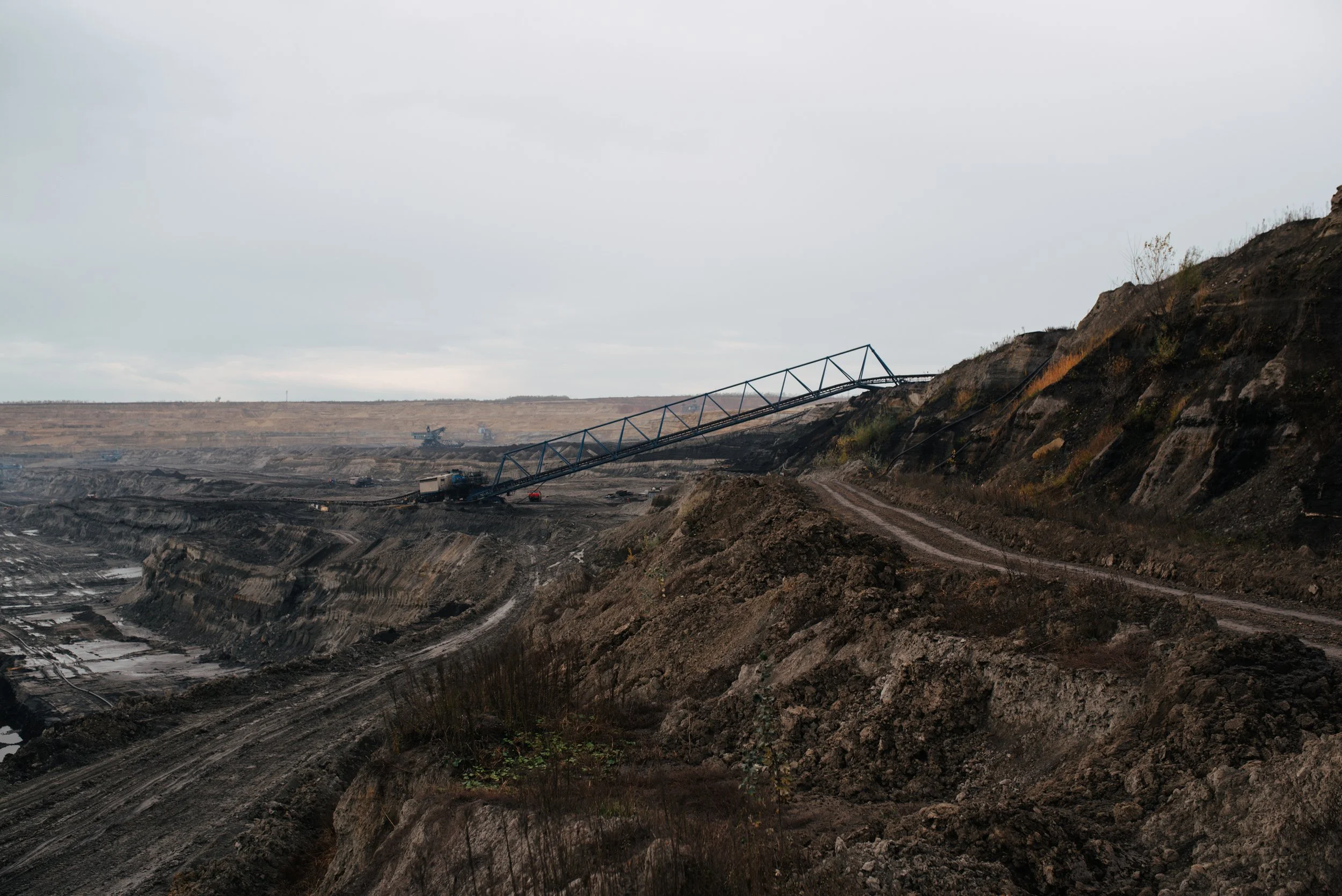 Bergwerk mit Förderanlagen und Abraumhalden bei Minenabbau, dunkler Himmel, staubige Umgebung