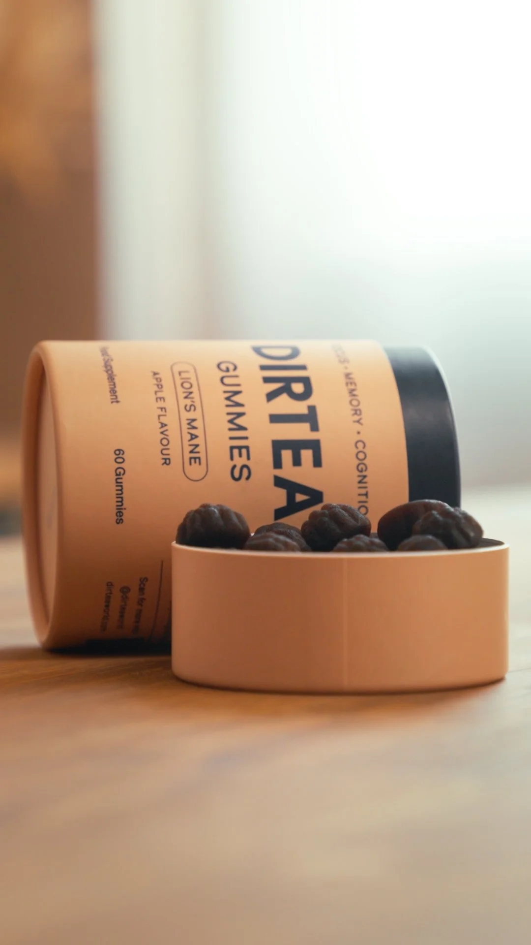 A container of gourmet gummies with a black lid, lying on its side with some gummies spilled out into a small bowl in front of it, on a wooden surface.